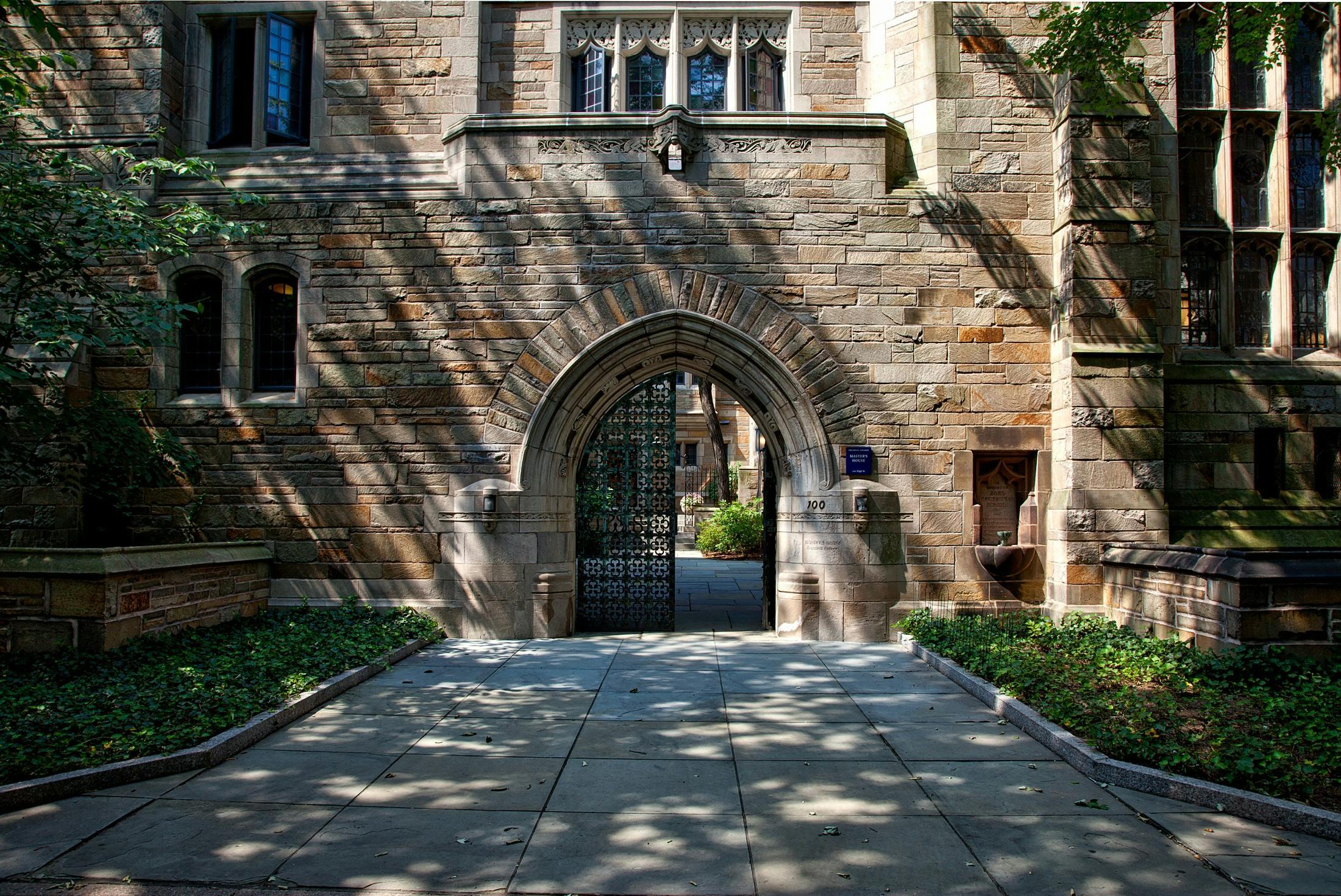 An arched entryway in an historic building is shown, cast in shadows and sunlight.