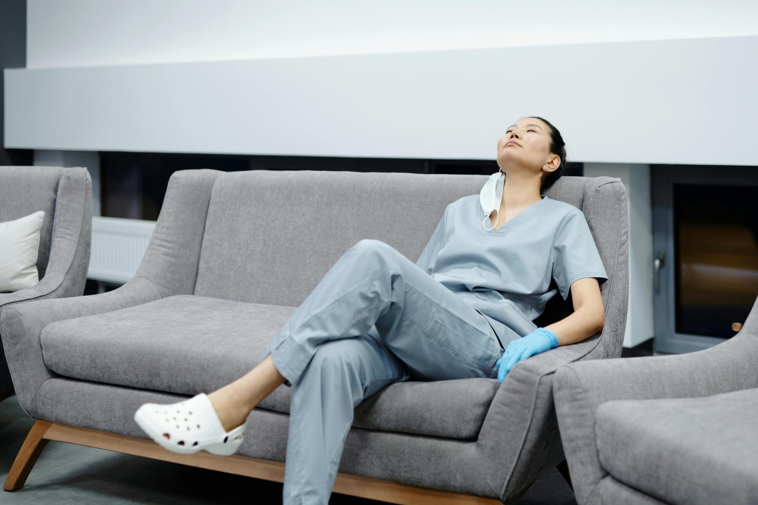 a nurse reclines on a gray couch, tired but satisfied from her work. 