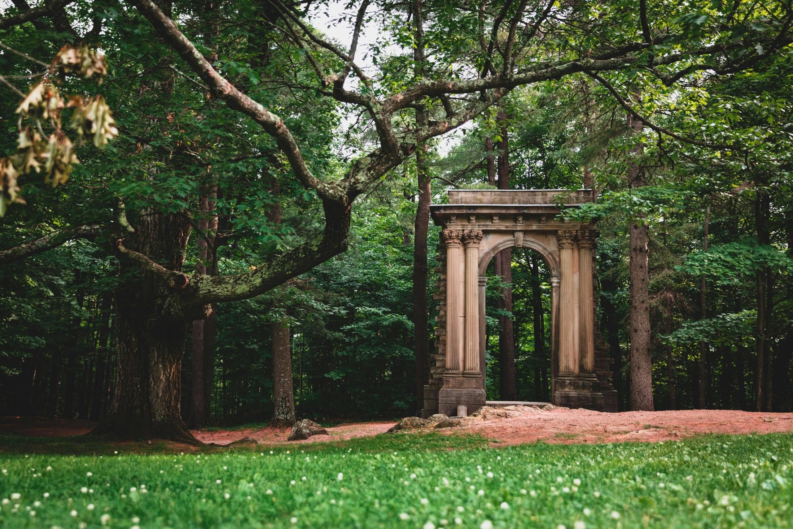 An ancient stone archway stands surrounded by green trees in Gatineau Park. The structure is part of the ruins at the MacKenzie King Estate.
