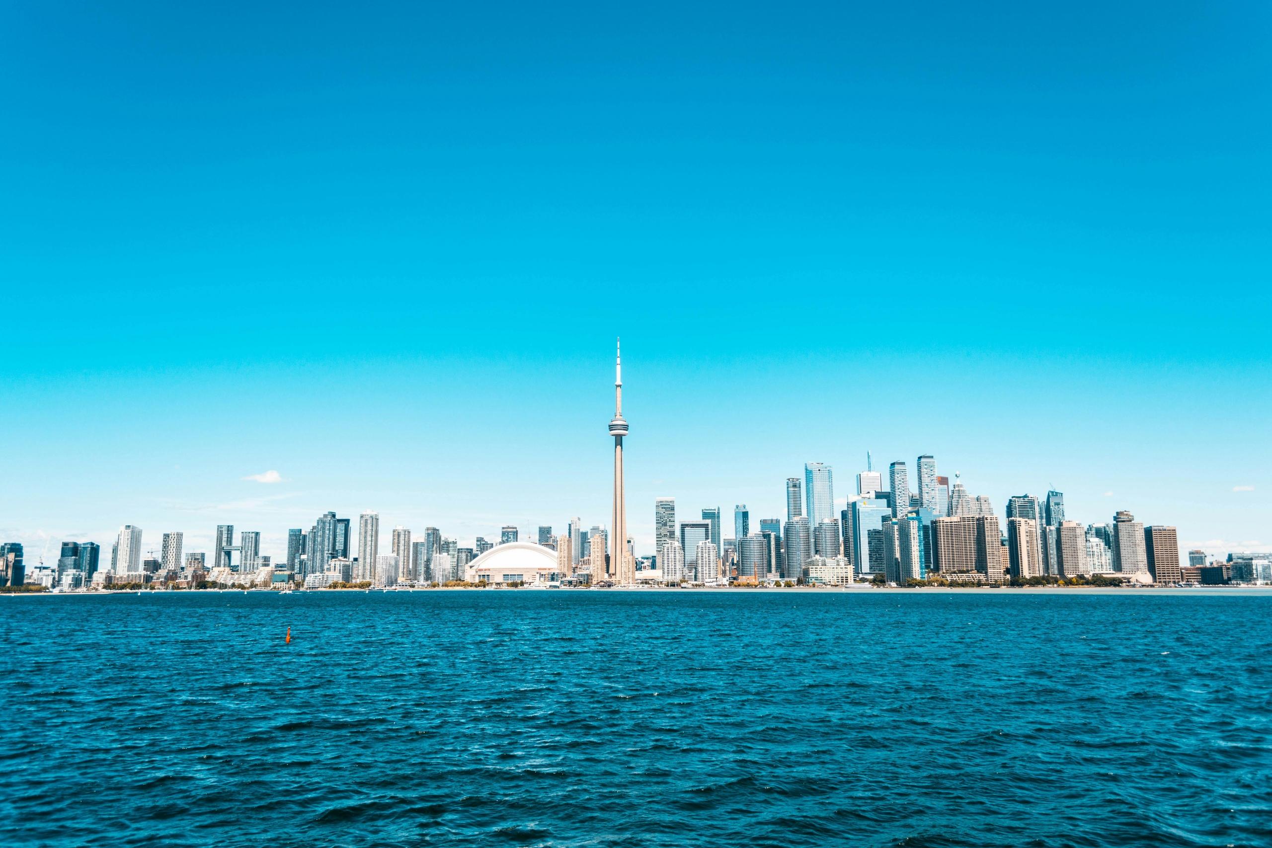 A photo of the Toronto skyline taken from across Lake Ontario. The sky is blue overhead.