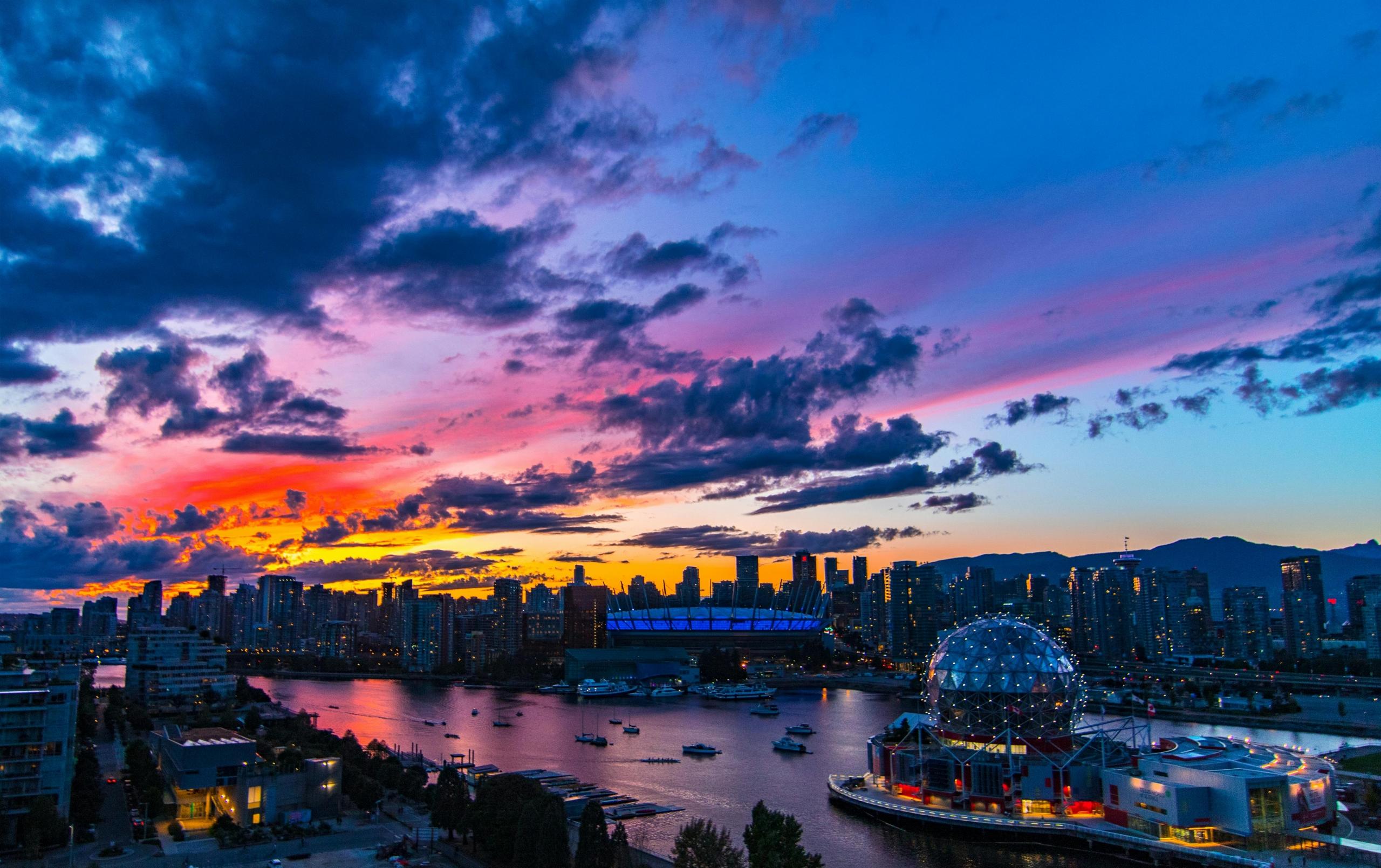 A photo of Vancouver at dusk. They olympic village can be seen. The sky is a mix of blue, pink, yellow, and is reflecting into the water below.