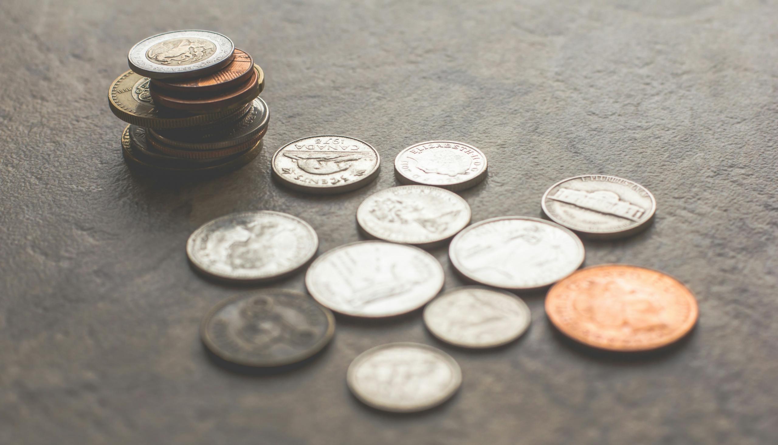 A close-up image of various Canadian coins, including nickels, dimes, and quarters, scattered on a textured surface.