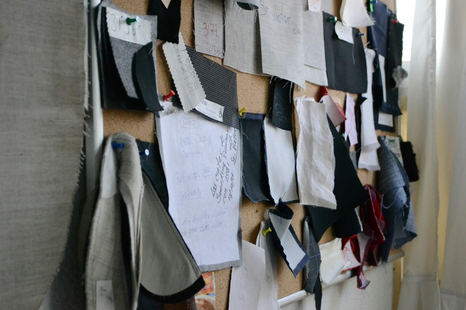 Corkboard covered with various fabric swatches and handwritten notes pinned with colorful pushpins.