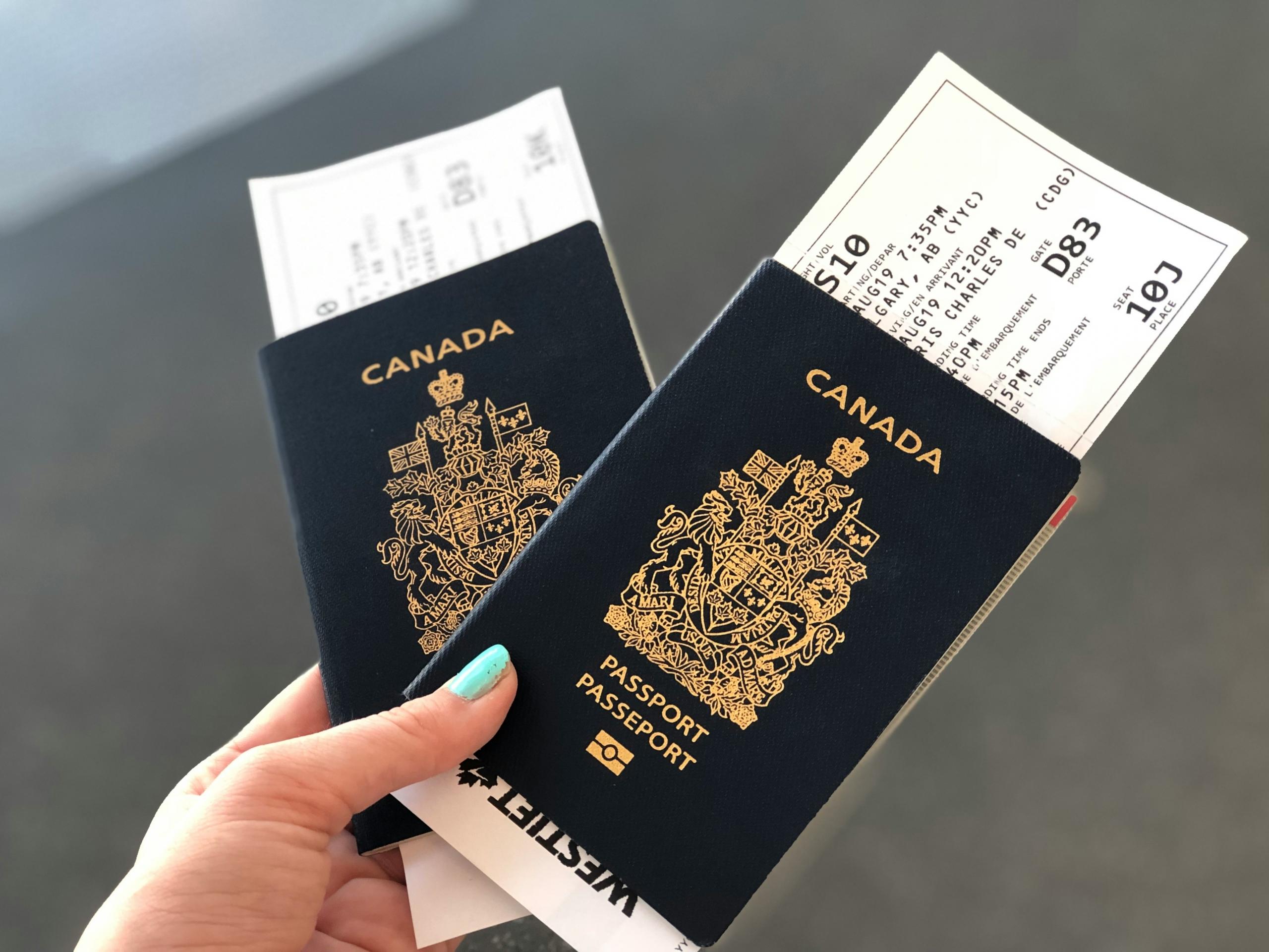 Two Canadian passports, prominently displaying the country’s Coat of Arms in gold, are held by a hand, with boarding passes peeking out from the top, symbolizing Canadian identity and travel.