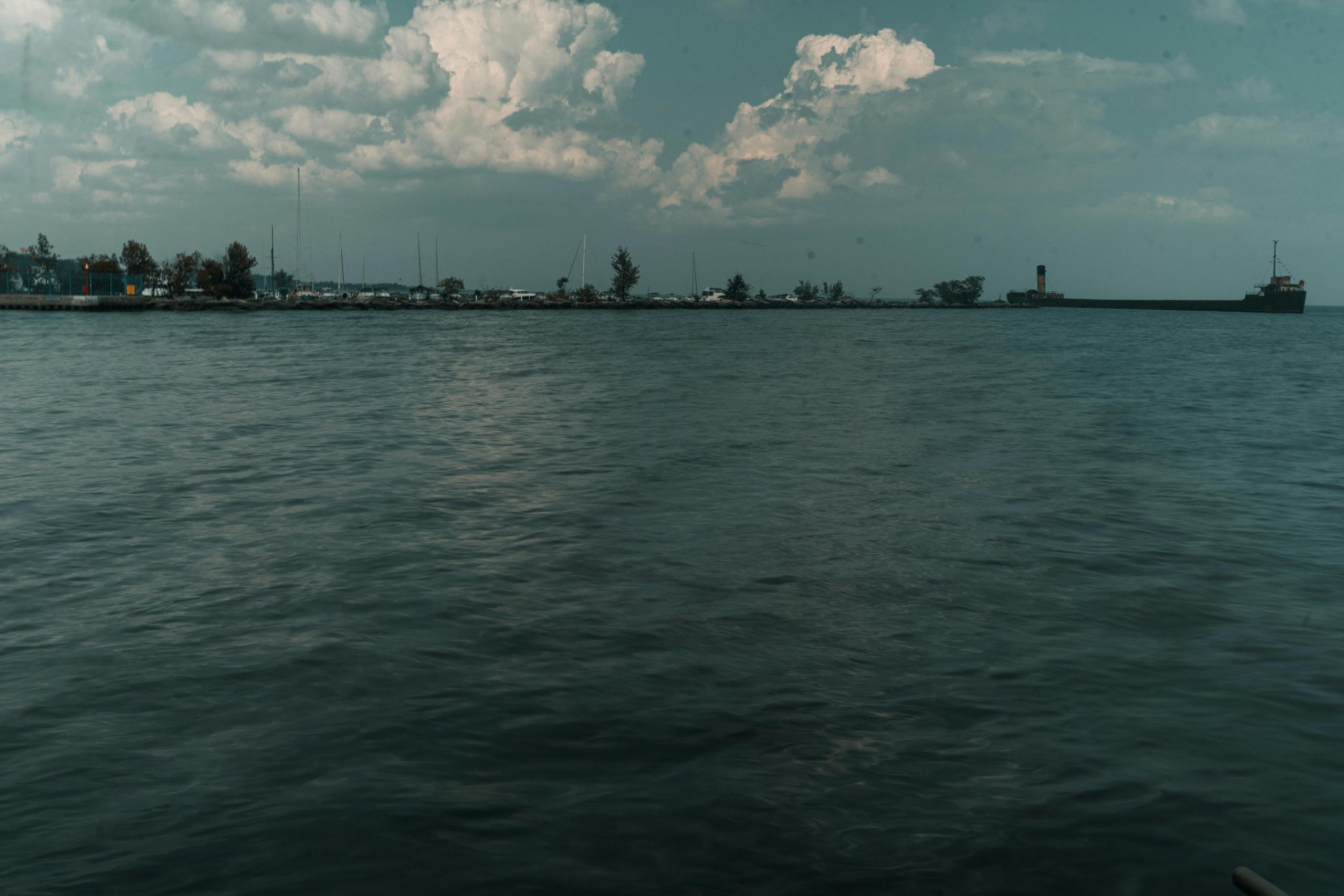a lake with dark waters. A shipping vessel can be seen in the background, along with a marina.
