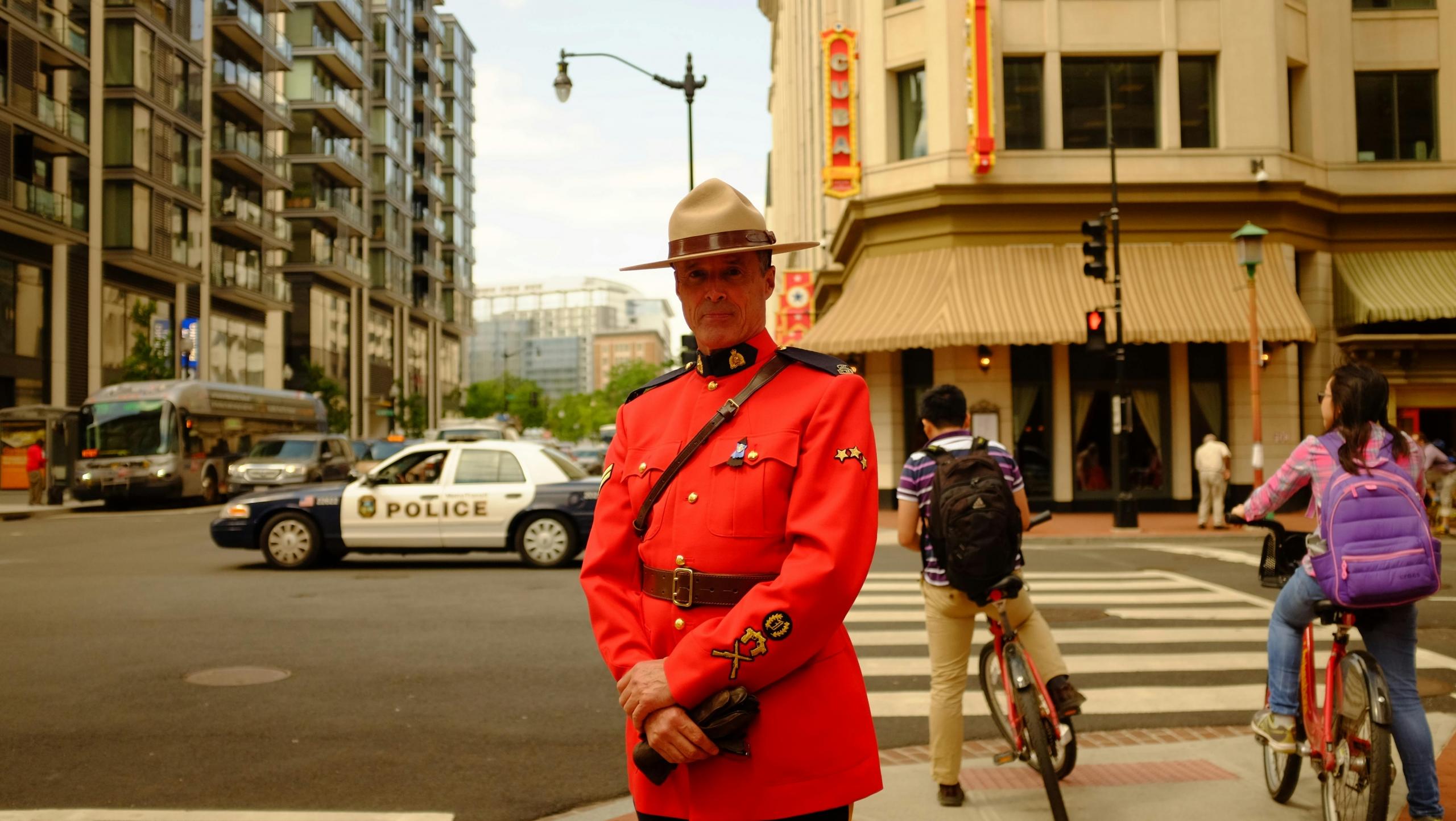 A Royal Canadian Mounted Police officer in red serge uniform standing in an urban setting.