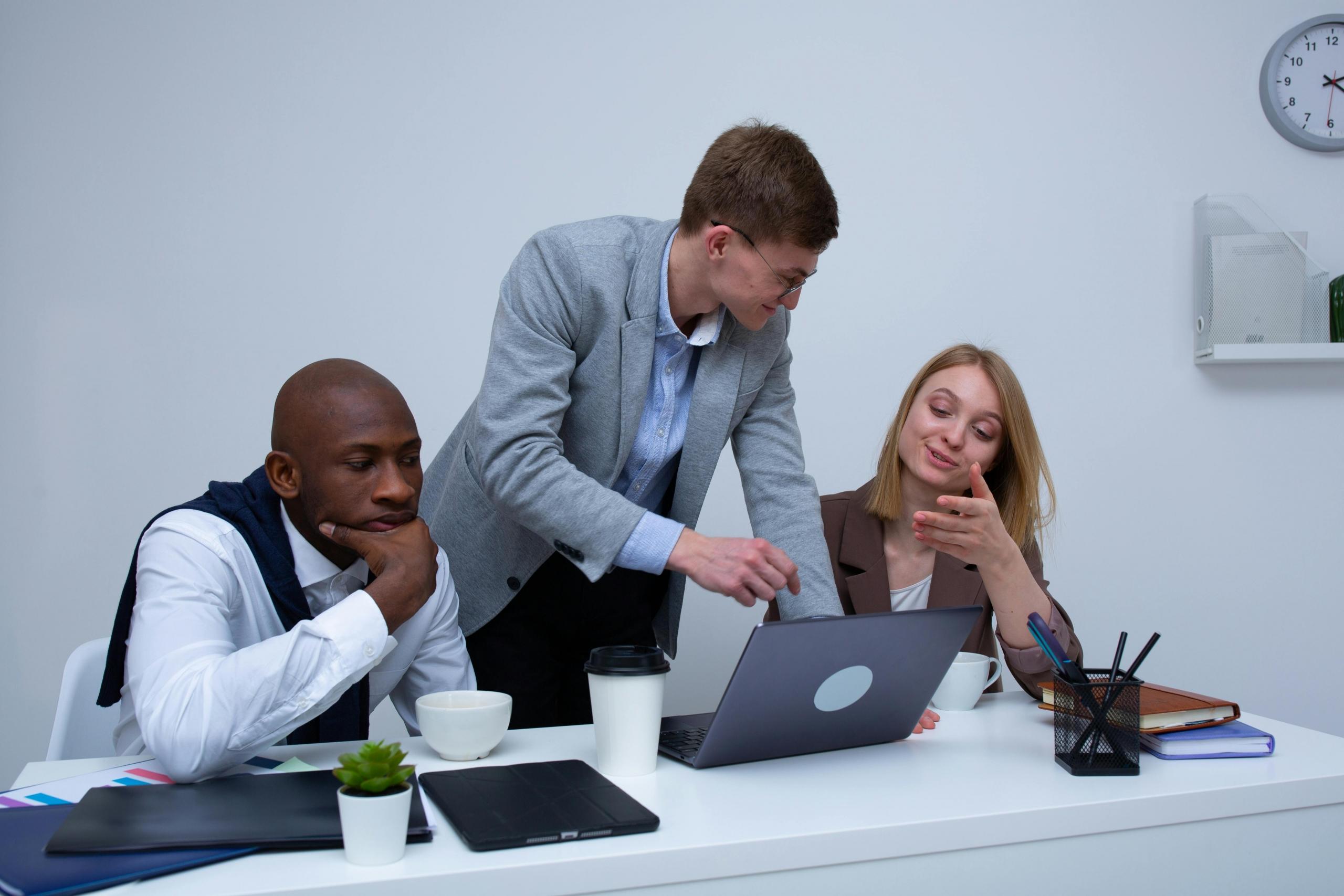 Three colleagues discussing work over a laptop in a meeting room.