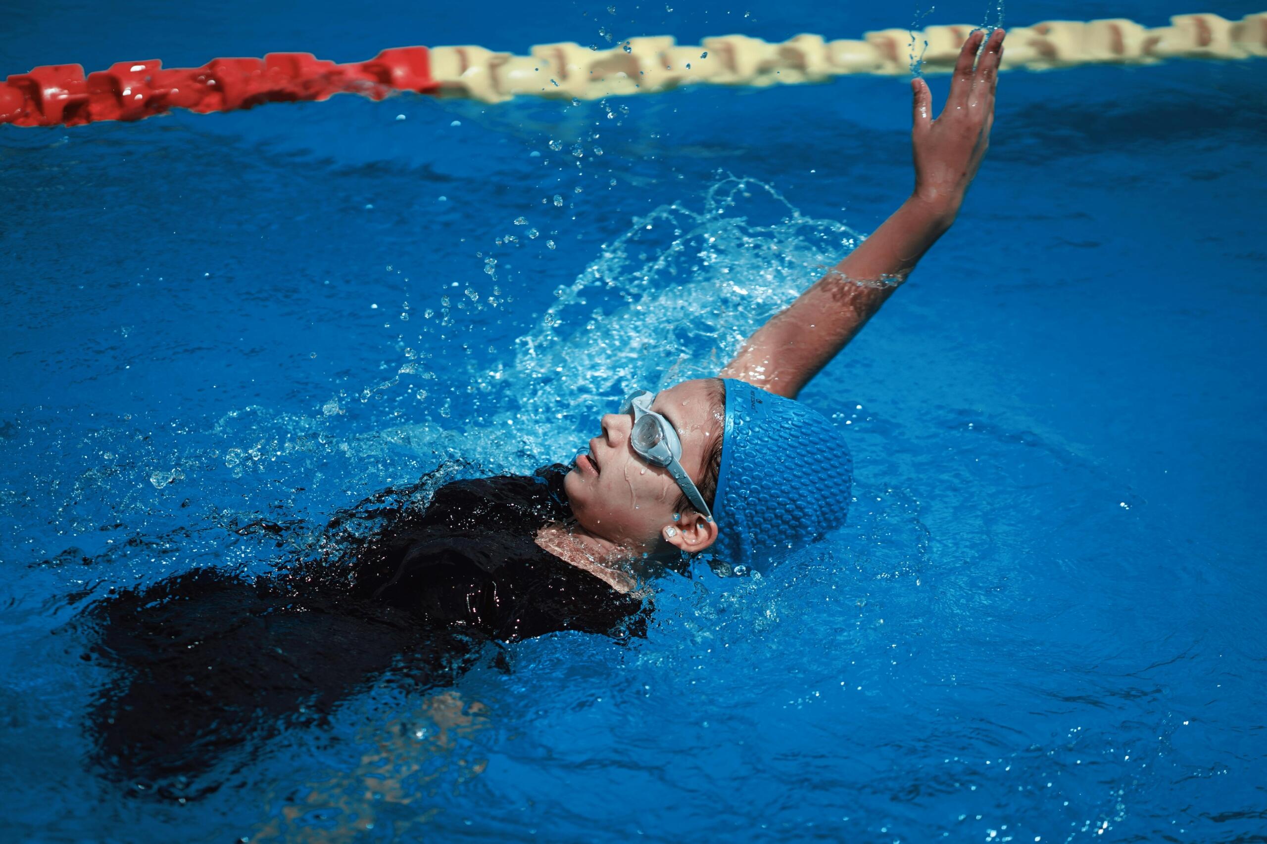 A swimmer in a blue swimsuit and cap strokes through clear aqua water, creating splashes around them.