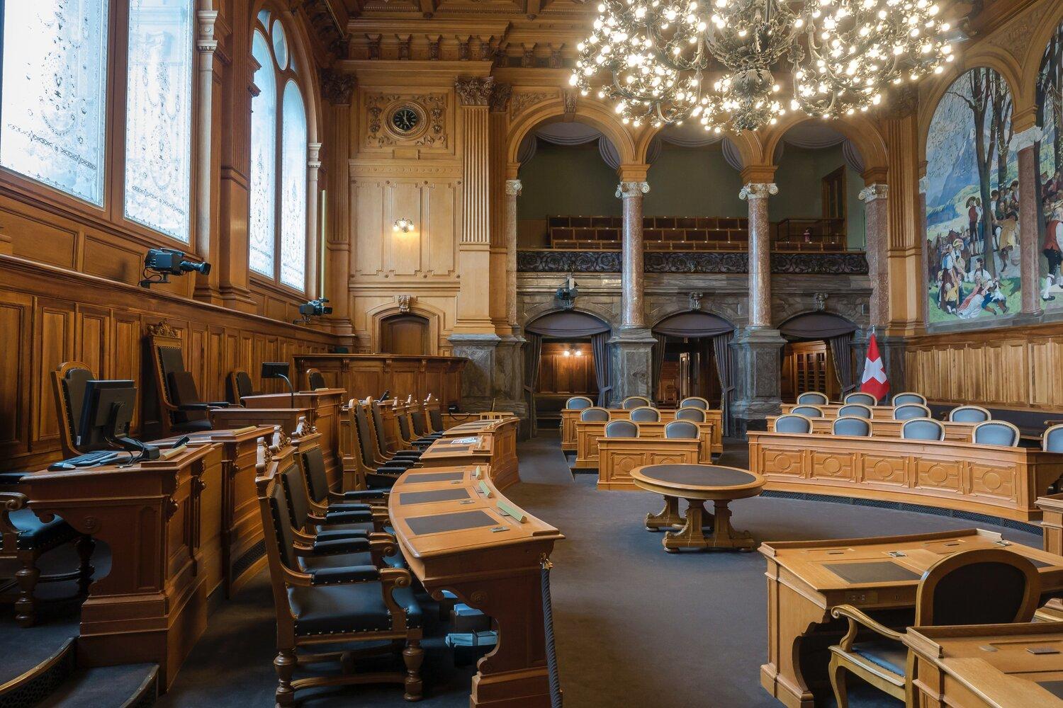 The photograph shows an empty courtroom with an elegant and antique decoration, slightly illuminated.