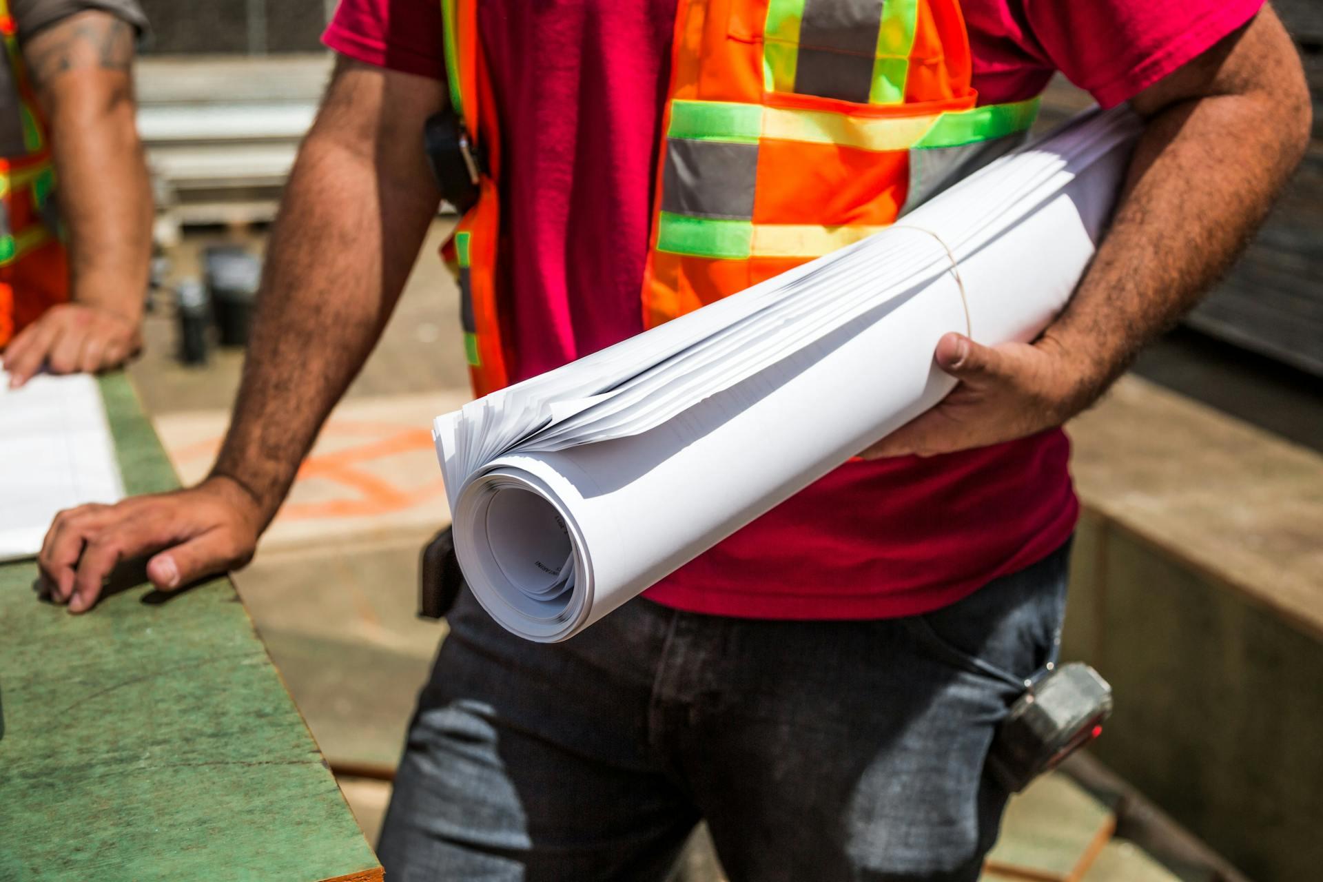 Person Holding Drafting Paper during Construction Project. 