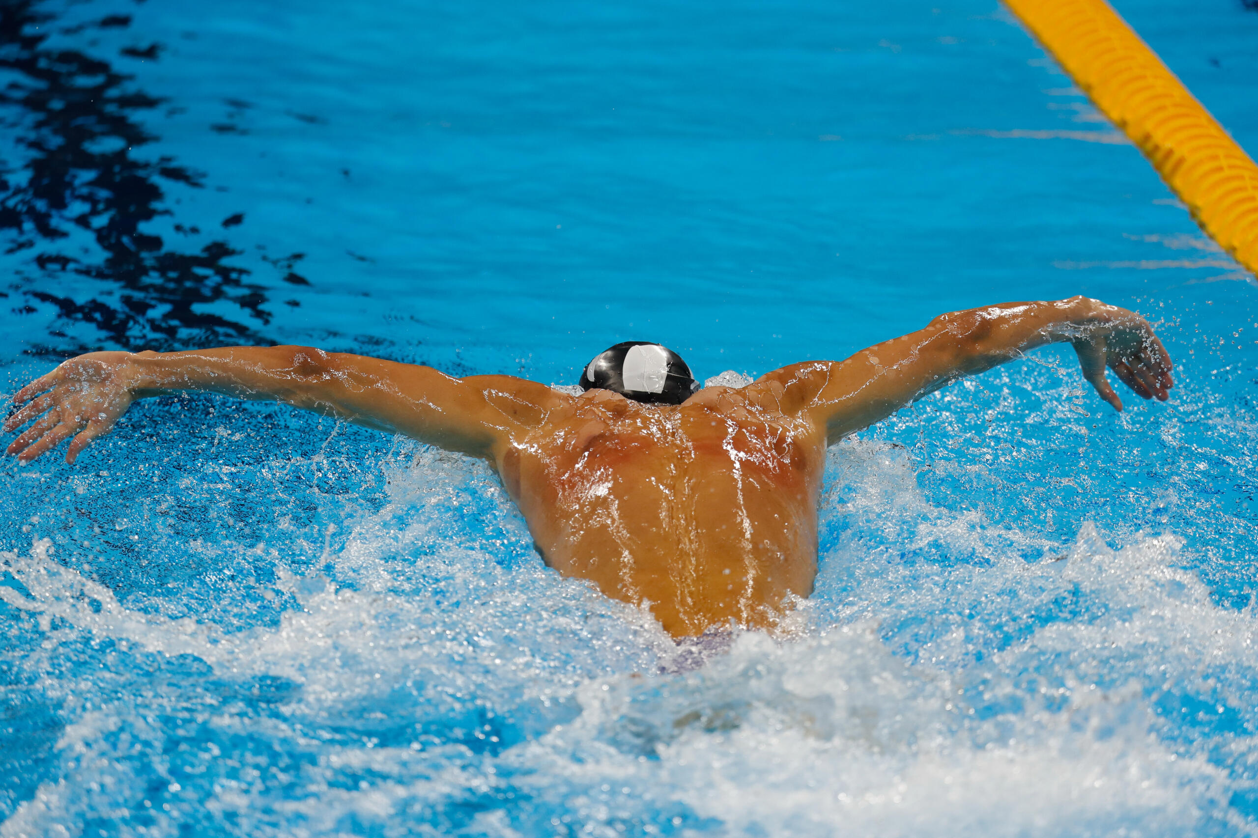 Michael Phelps performing the butterfly stroke in a pool, creating splashes of water behind them.