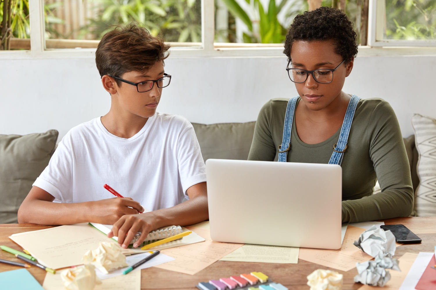 a young student taking notes while his tutor is looking a laptop