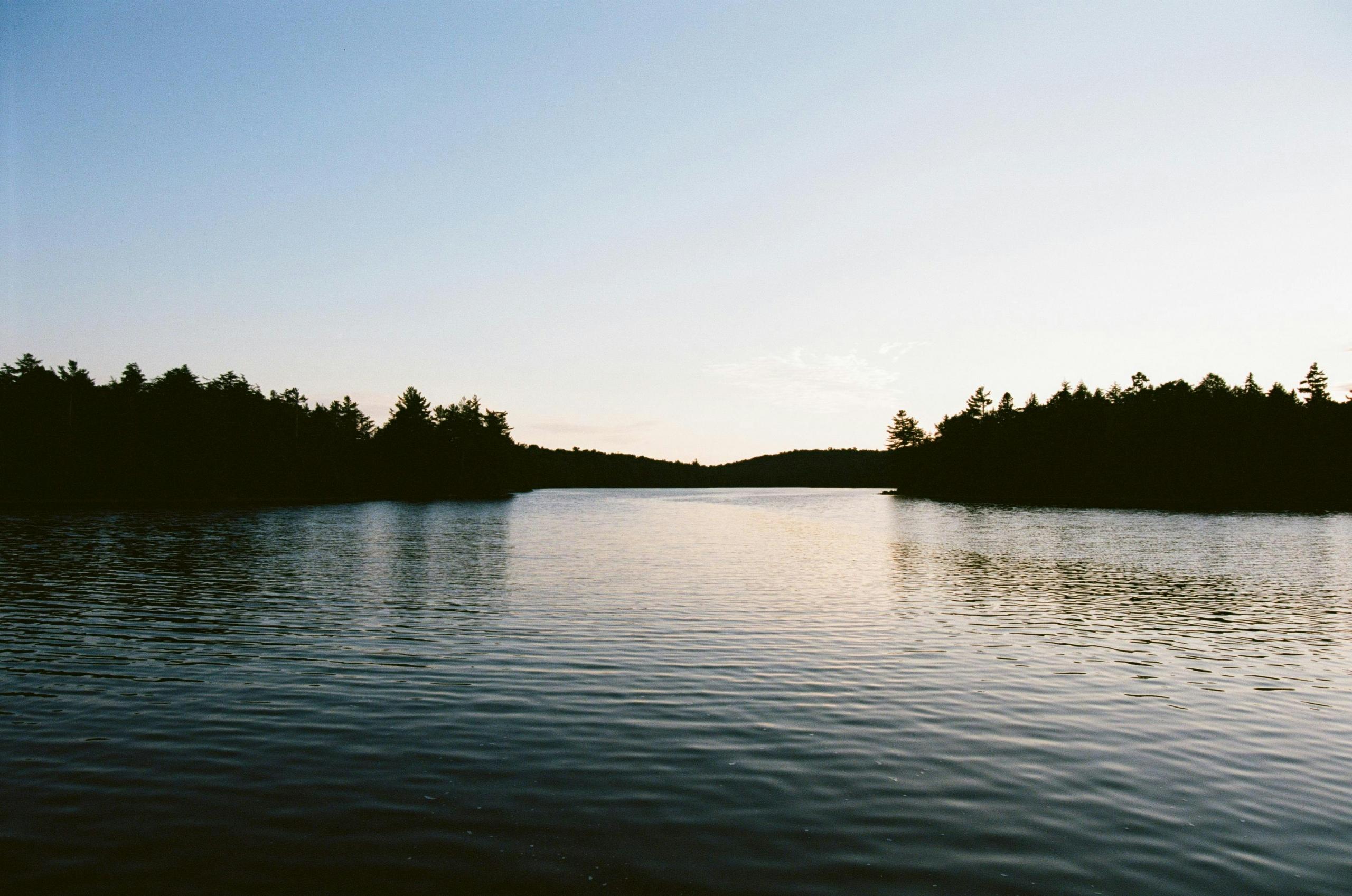 A peaceful lake at sunset surrounded by trees in Algonquin Provincial Park, Canada.