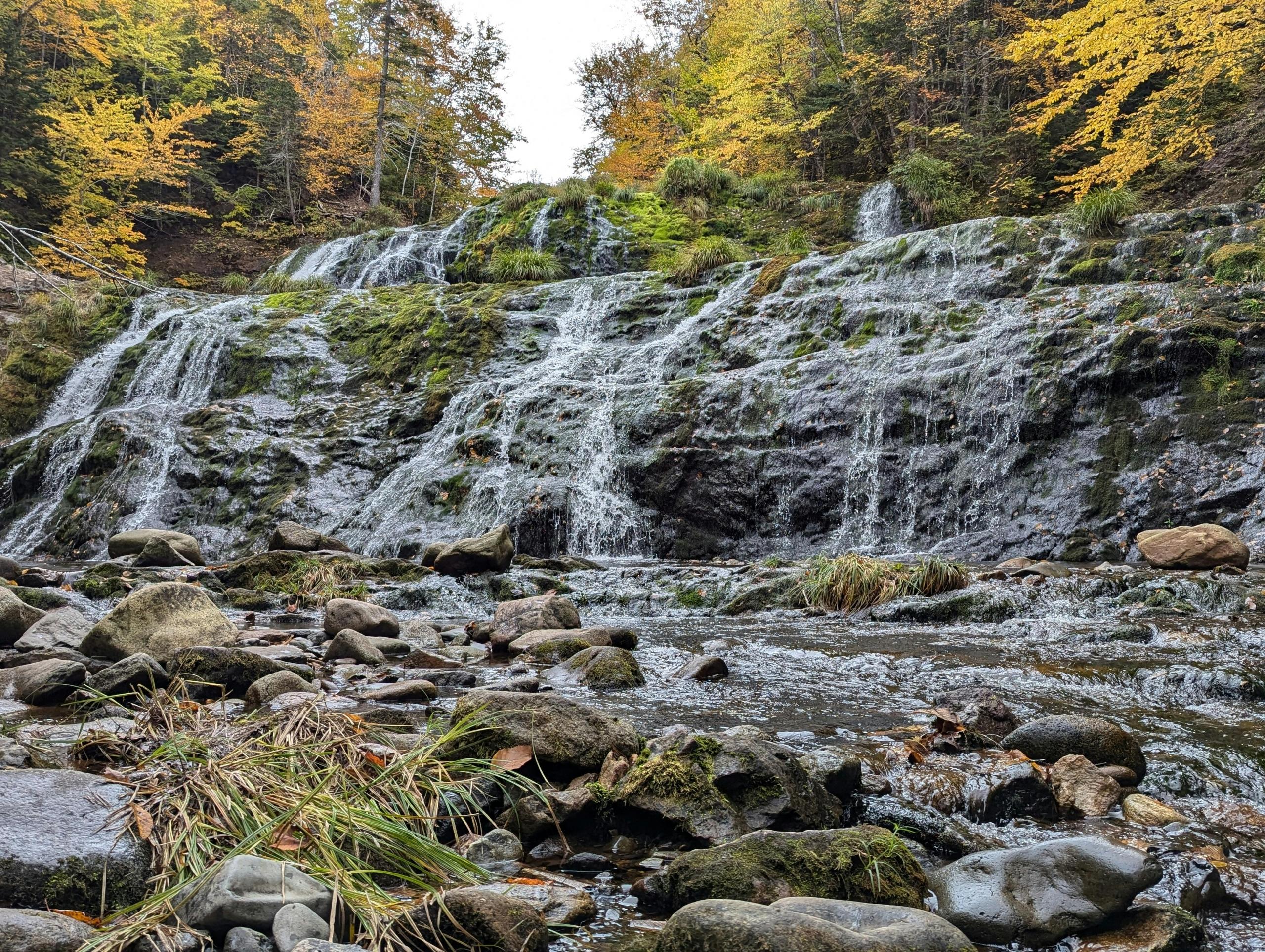 Waterfalls flowing over mossy rocks surrounded by fall foliage in a Canadian national park.