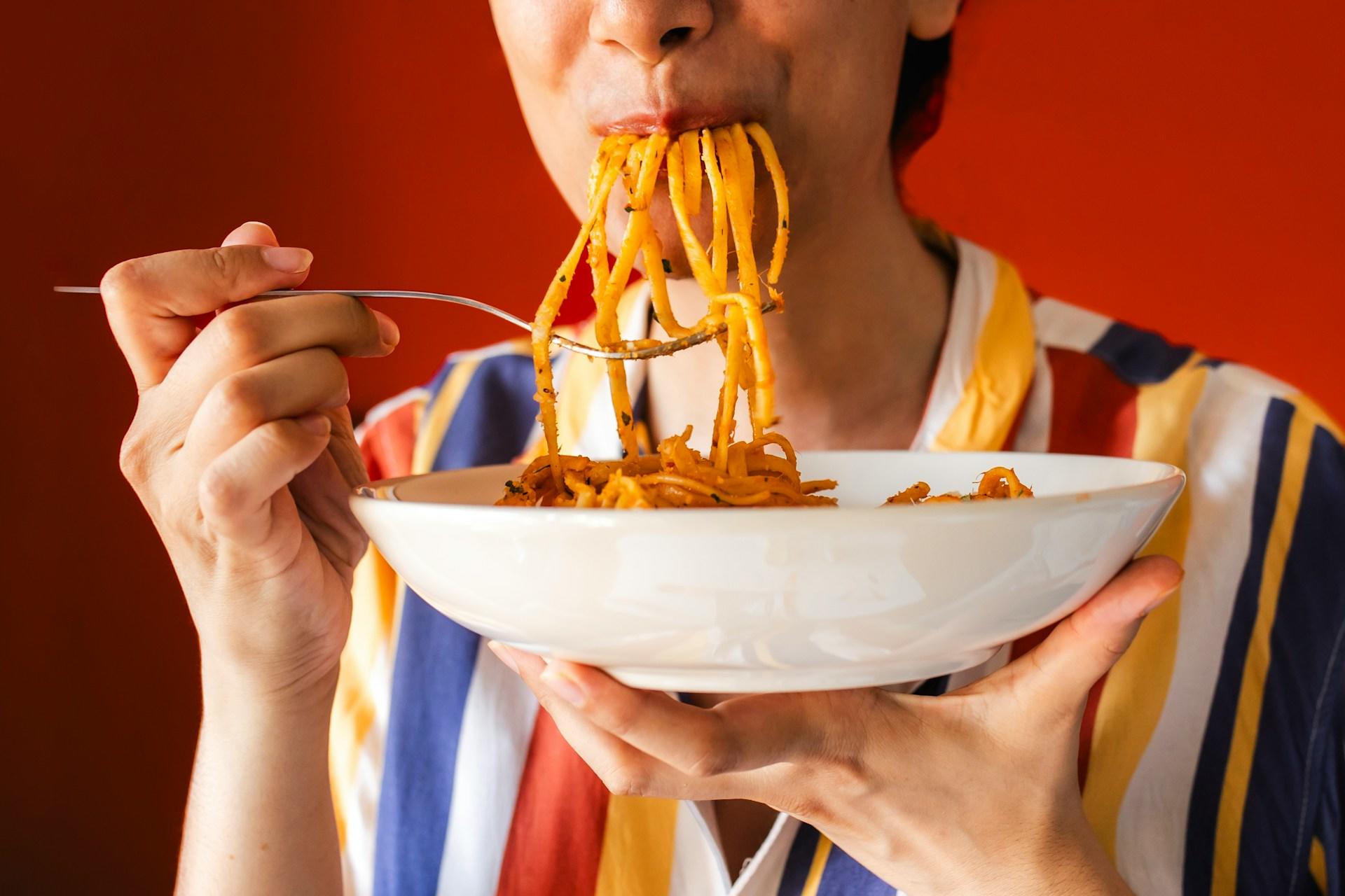 A person eating a mouthful of the linguine pasta with a fork. 