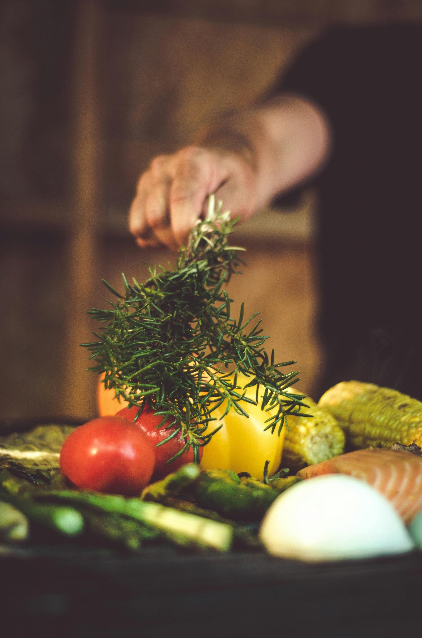 a chef places herbs on a tray of vegetables and salmon.