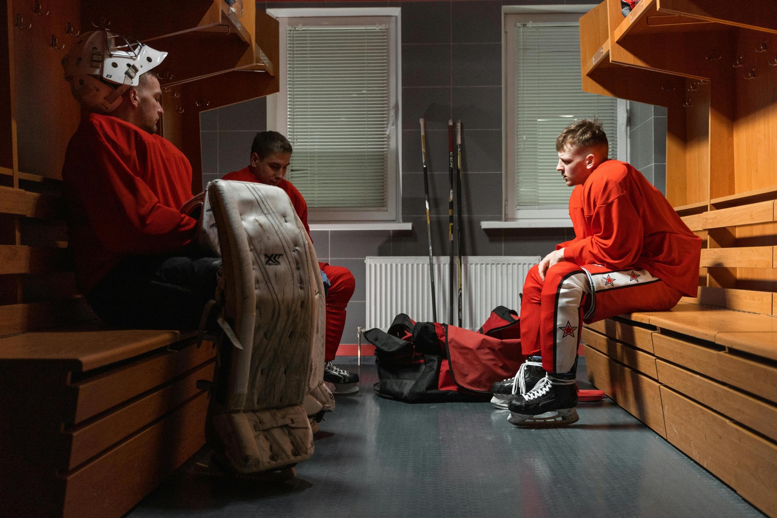 hockey players sit in a change room with wooden benches.