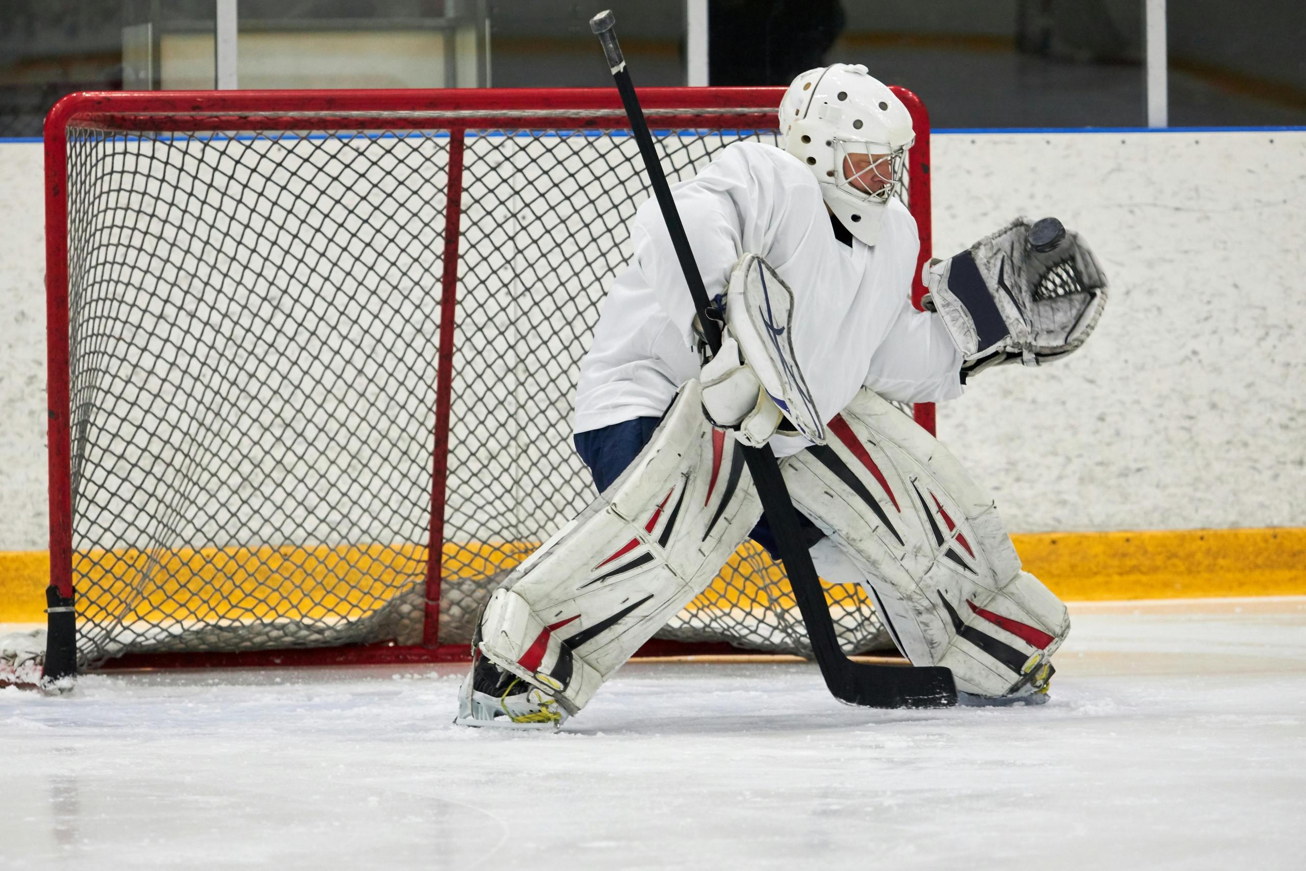 a goalie stands in the hockey net. He wears a white uniform