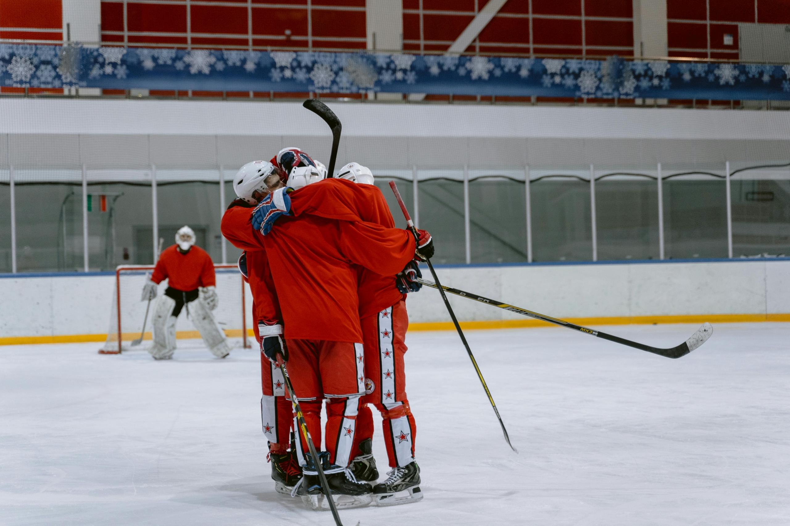 Hockey players in red uniforms embrace on the ice.