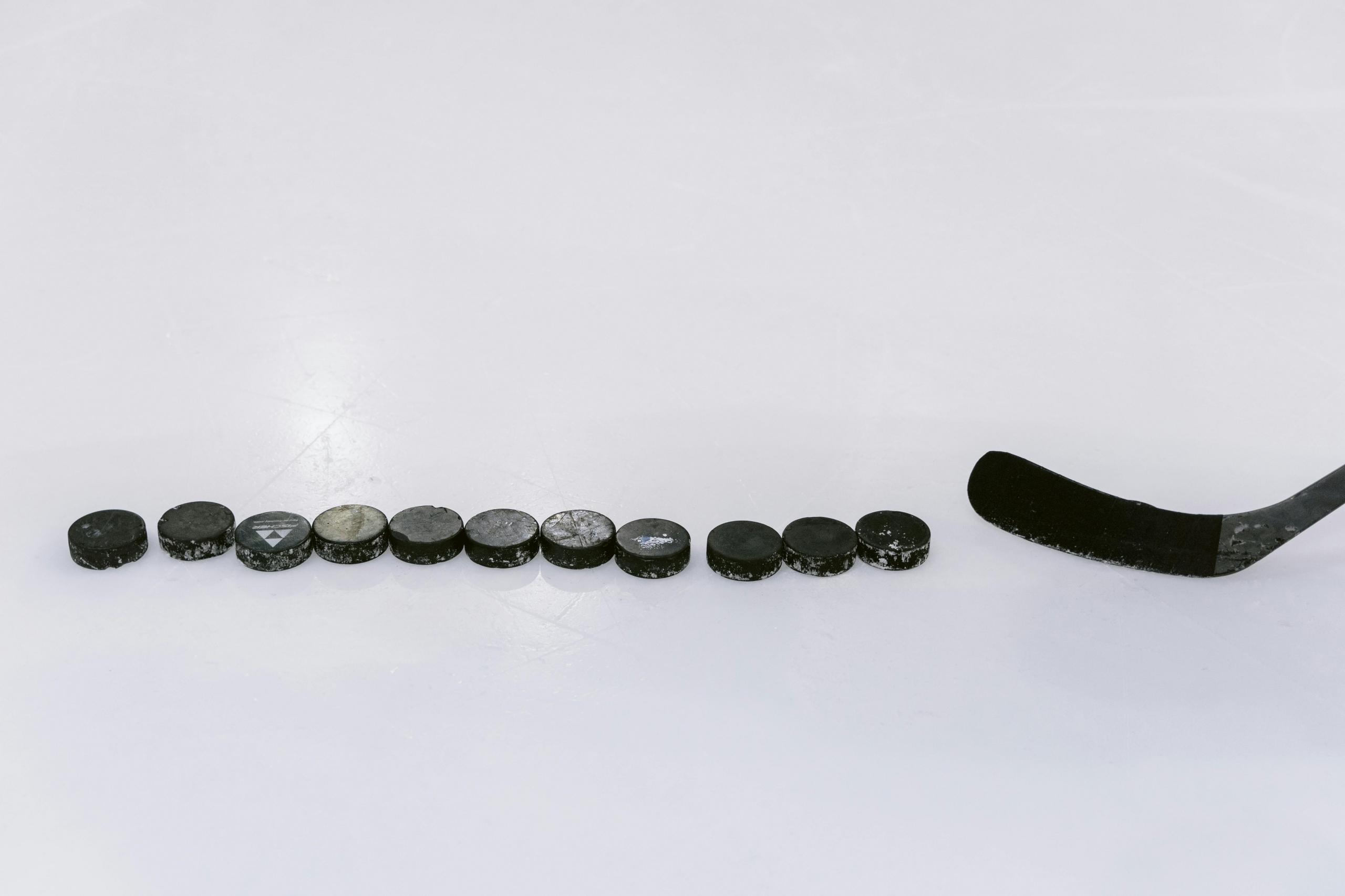 11 hockey pucks are on the ice. A stick is ready to shoot the pucks.