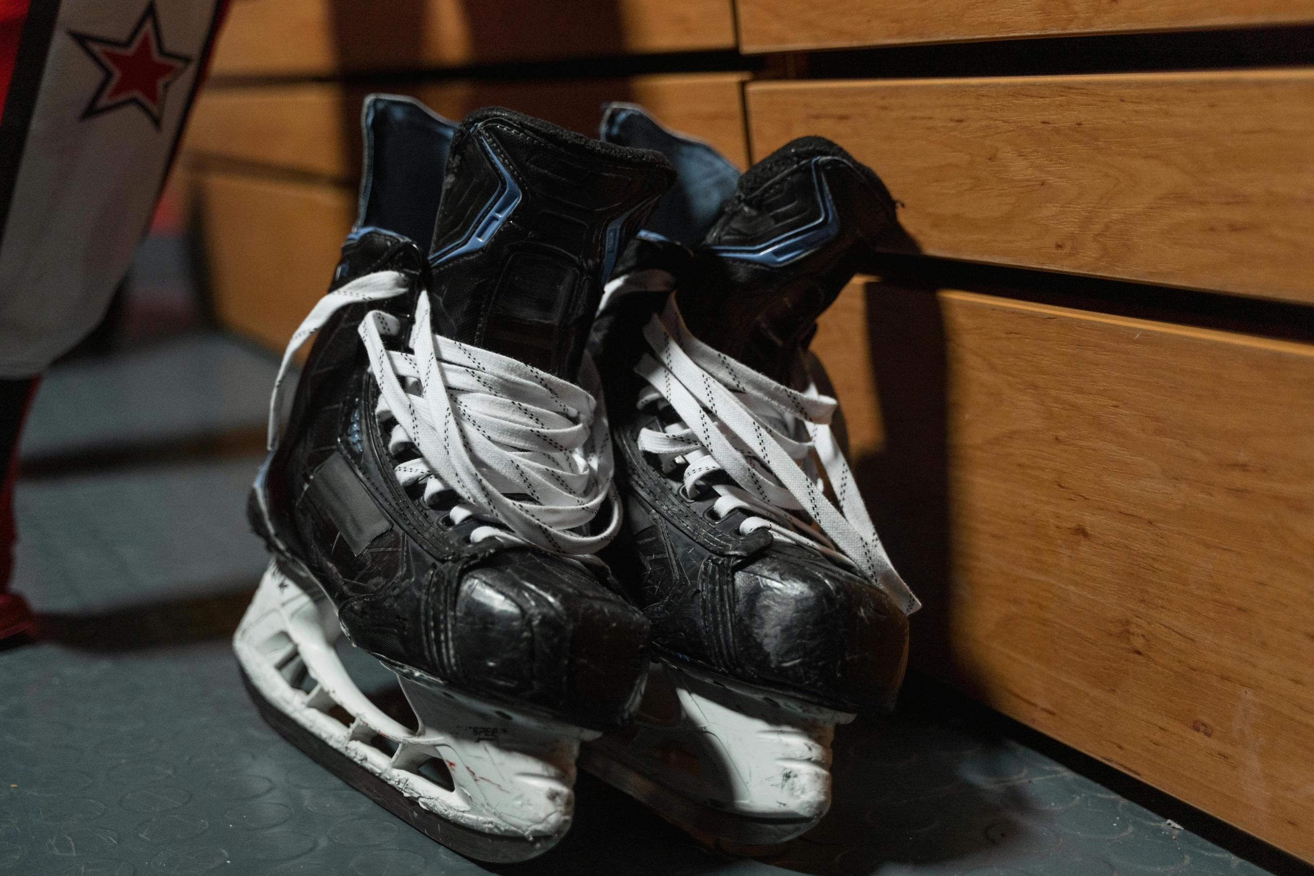 a pair of black hockey skates lean up against a wooden bench.