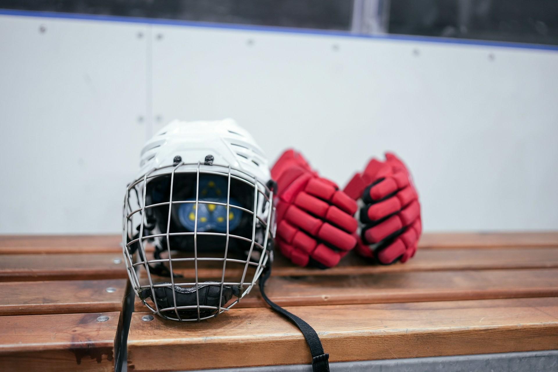 A white hockey helmet and red hockey gloves on the sideline bench