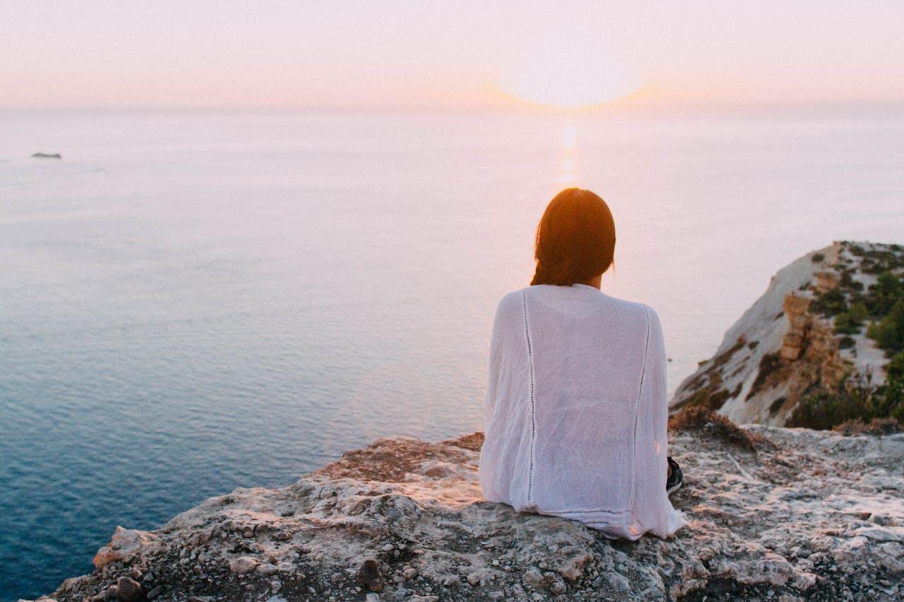 A women sitting on a cliff looking out into the ocean.