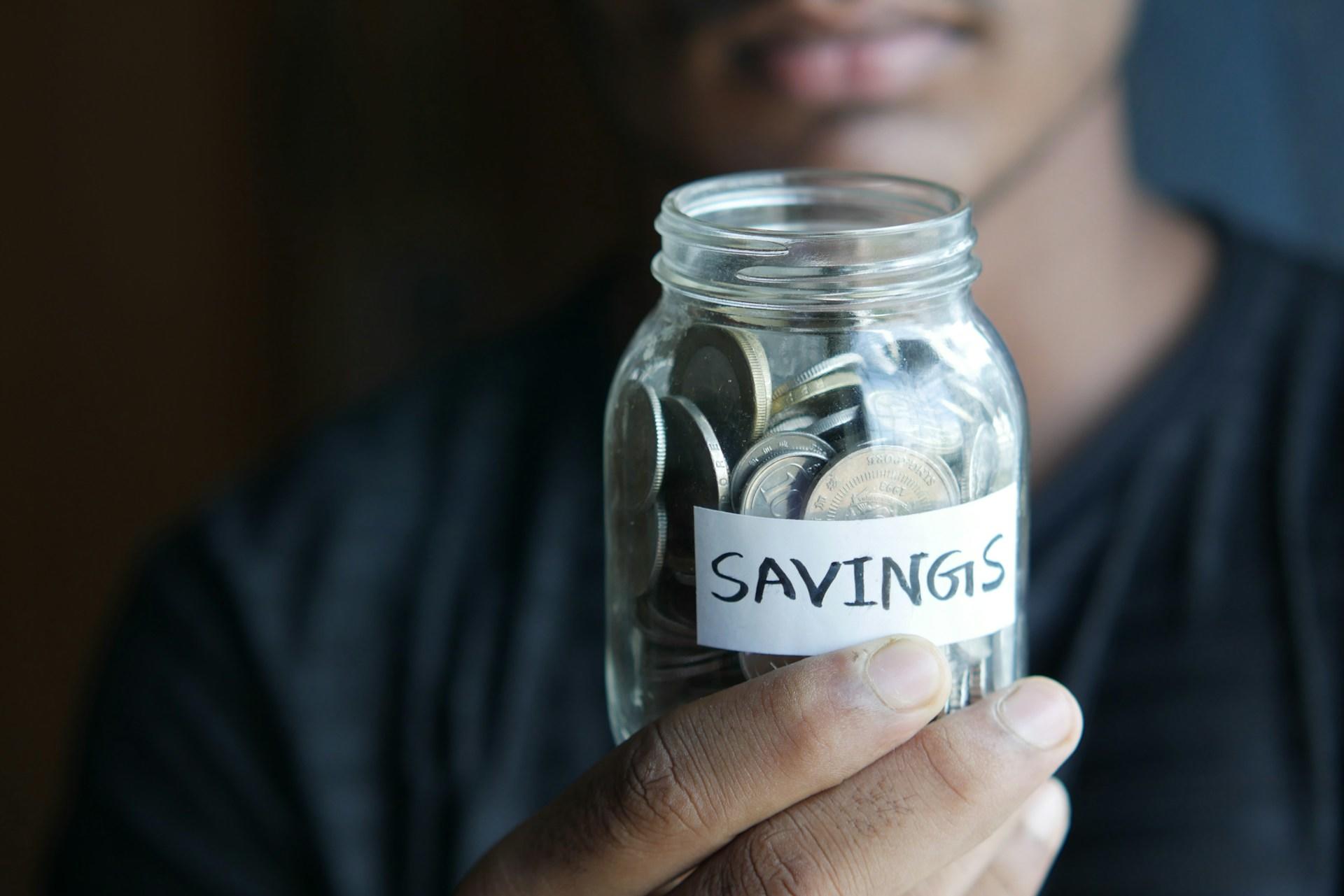 a person holding a container of coins with the label savings.