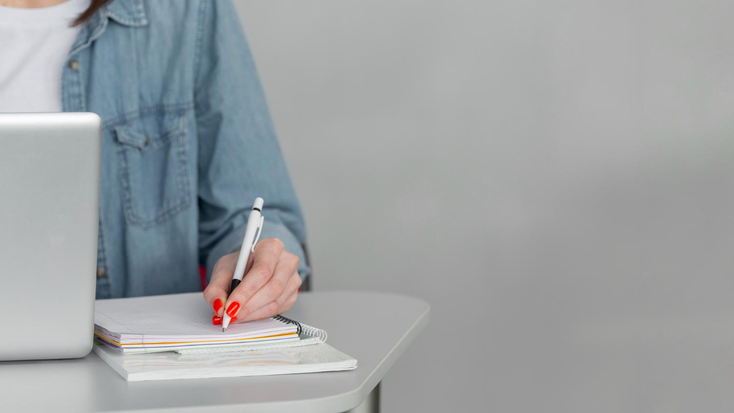 a student writing notes in front of a laptop