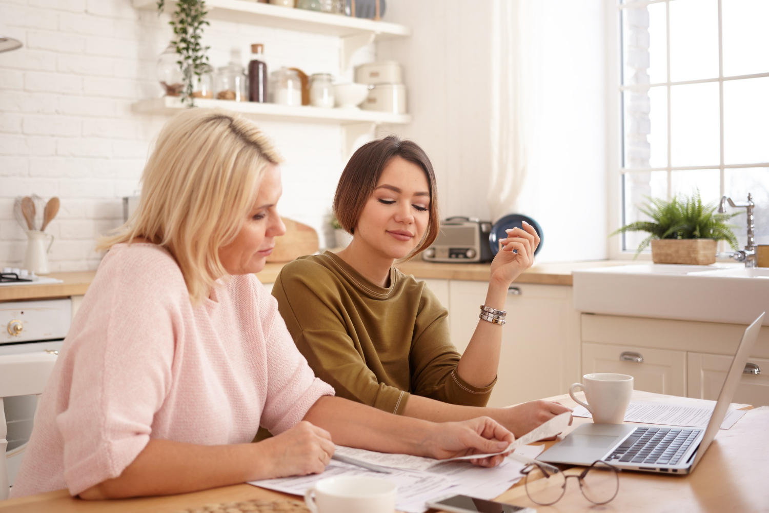 a tutor showing a student something on paper in front of a laptop.