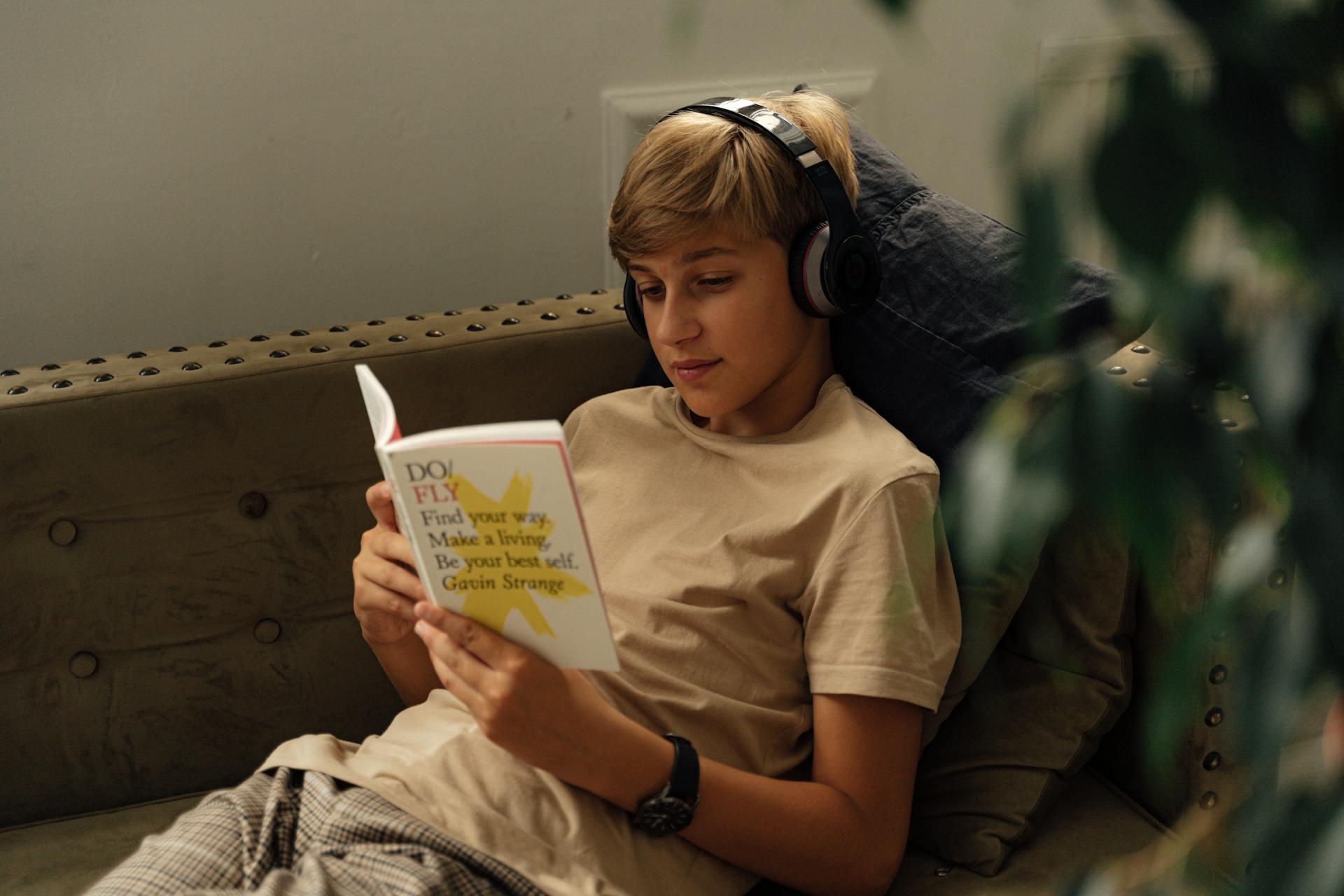 Person wearing headphones, sitting on a sofa and reading a book titled "Do Fly: Find Your Way, Make a Living" by Gavin Strange.
