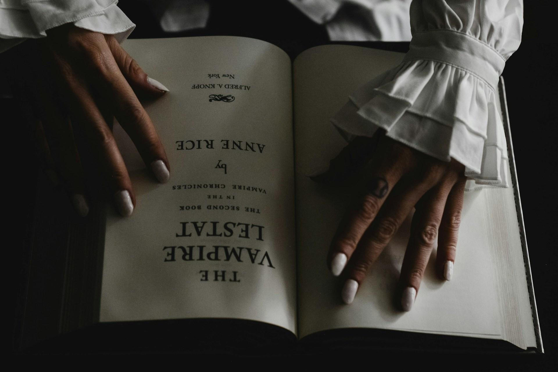 A lady's hand on a book called "The Vampire".