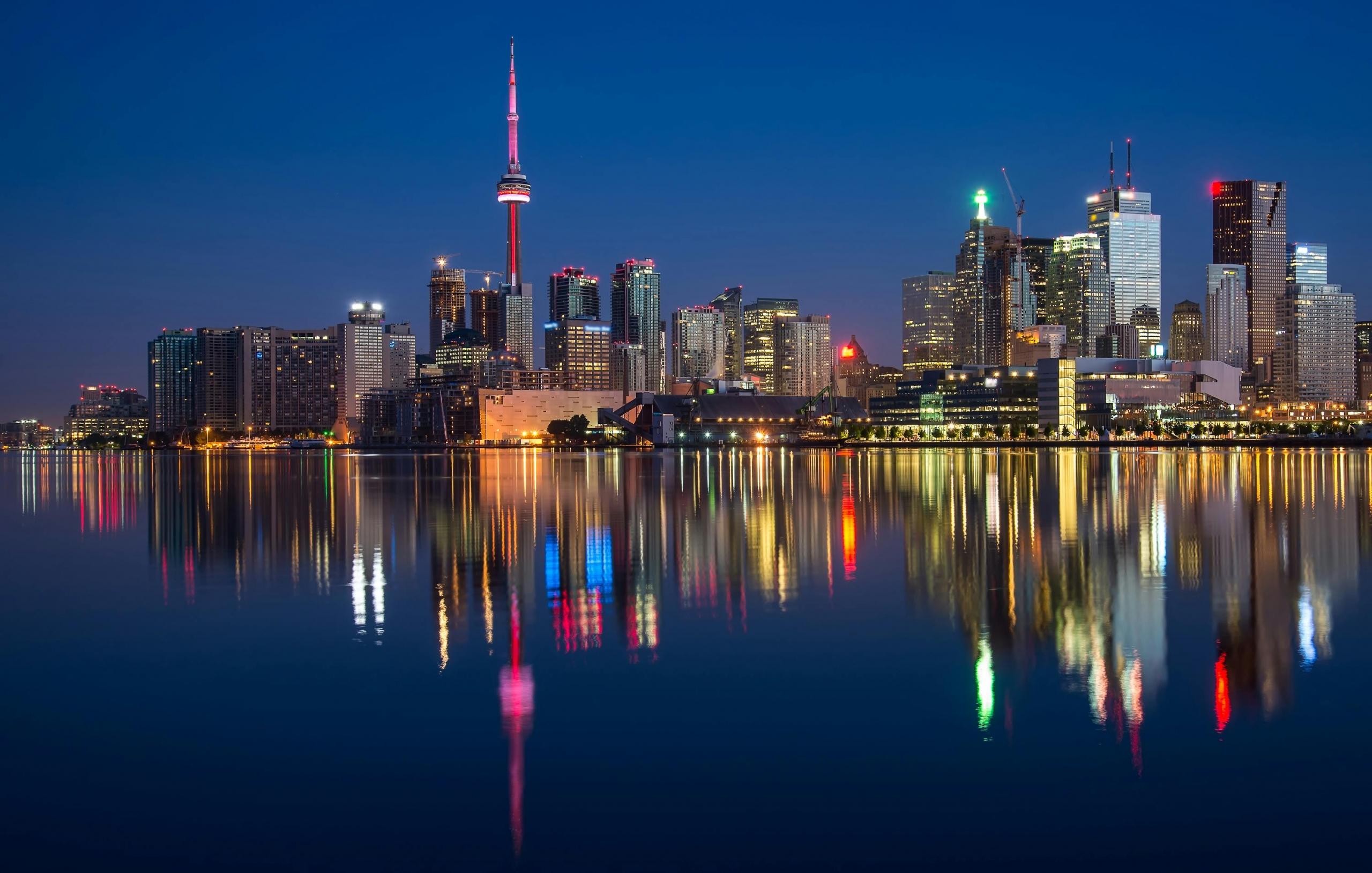 a photo of the Toronto skyline over the lake a dusk. The city reflects into the water.