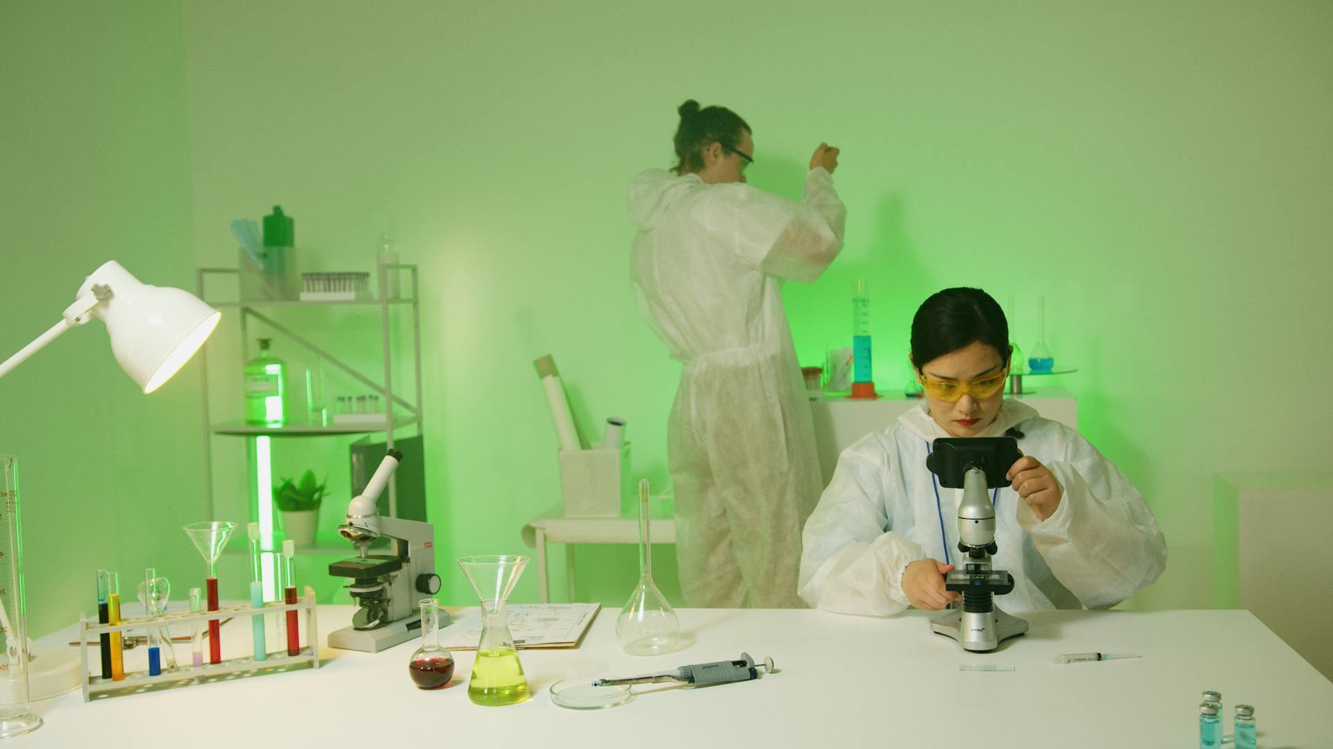A Woman using a Microscope in a room with green lights.