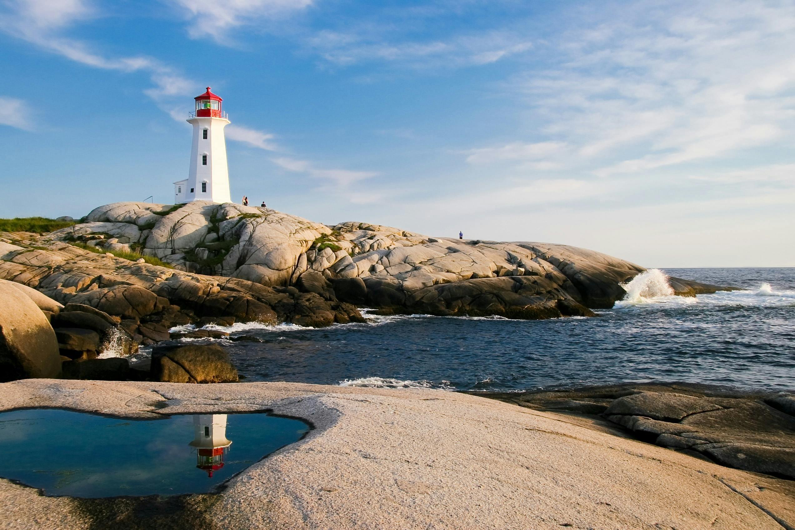 A white and red lighthouse stands on rocky coastline.