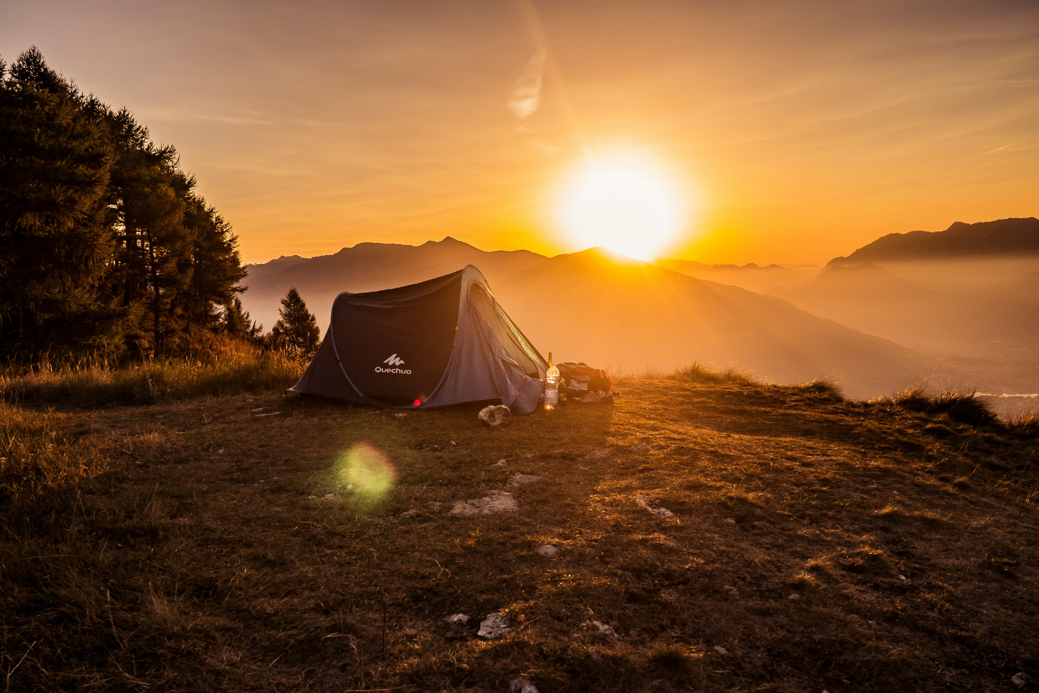 A camping tent set up on a grassy hill with a beautiful sunset over the mountains in the background.