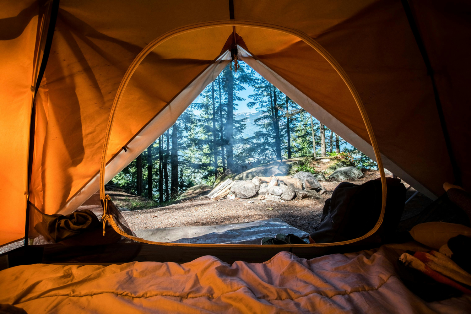 A forrest view can be seen framed by the opening of an orange tent.