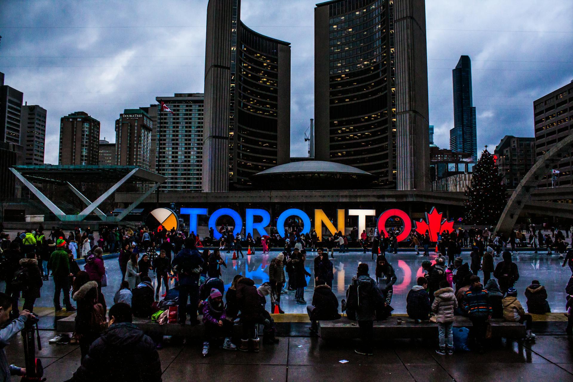 The picture shows downtown Toronto during Canada Day with a lit up sign spelling TORONTO.