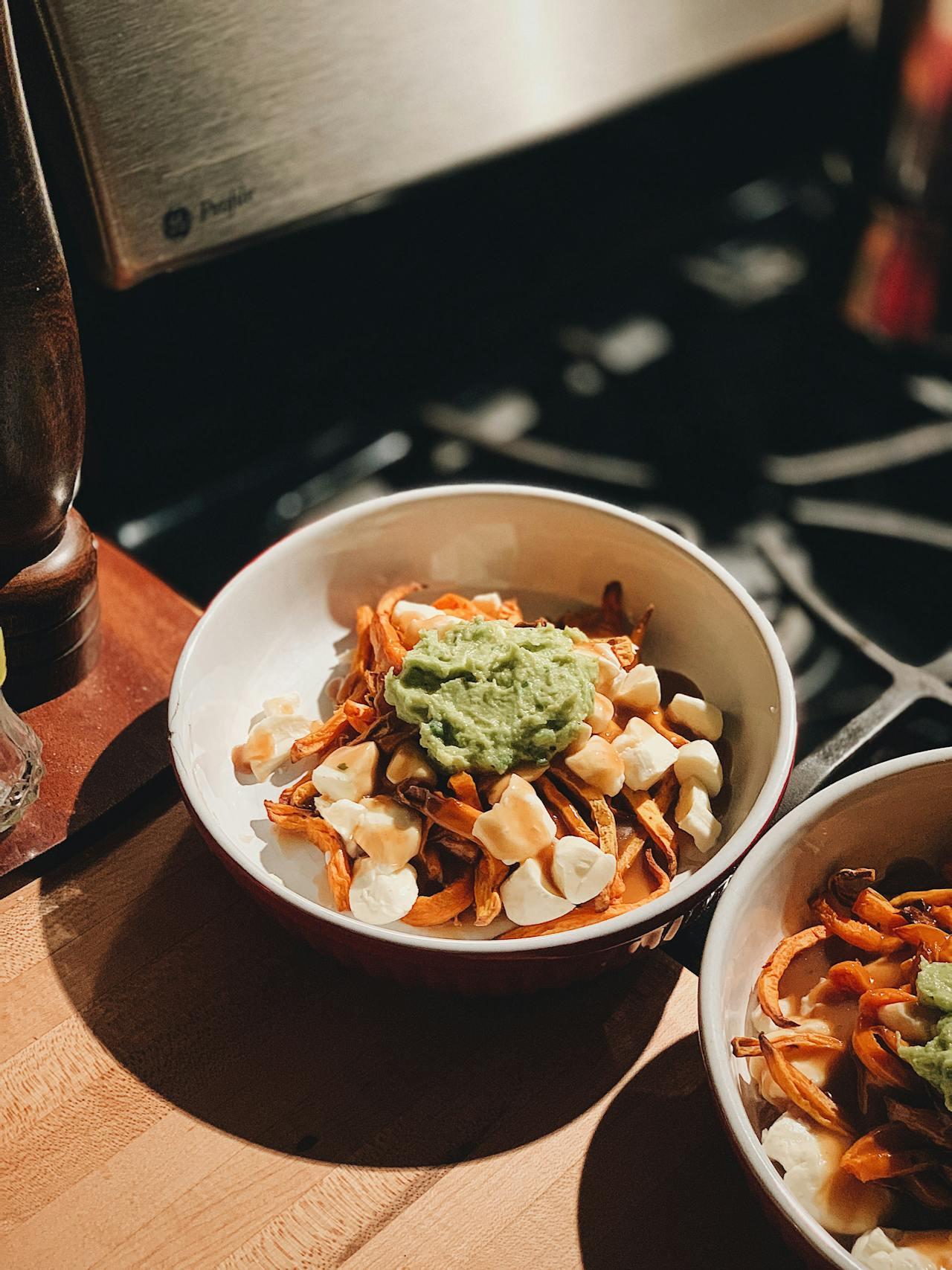 Two white ceramic bowls with poutine inside.