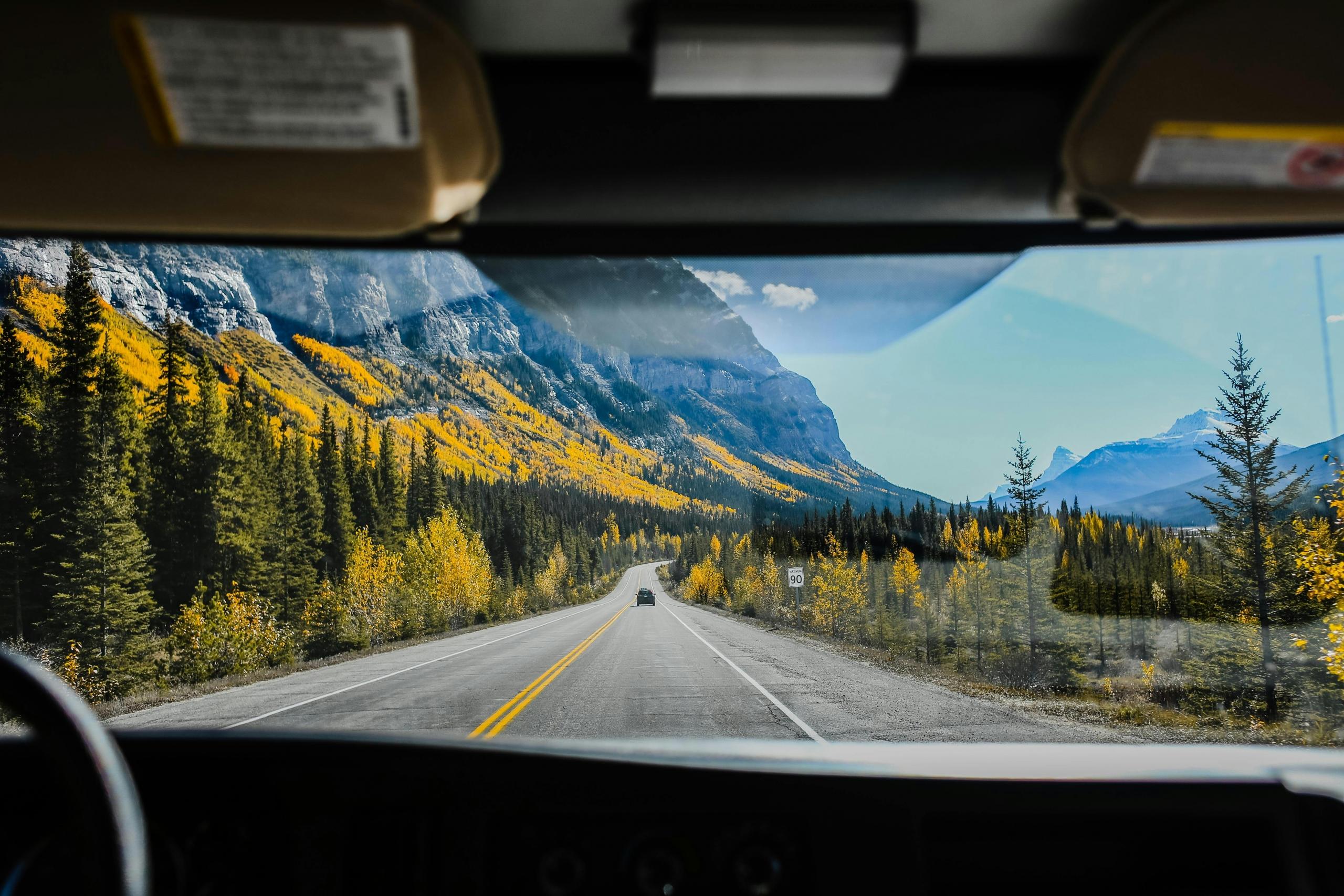 a driver looks through the front windshield. Mountains, forests, and blue skies can be seen.