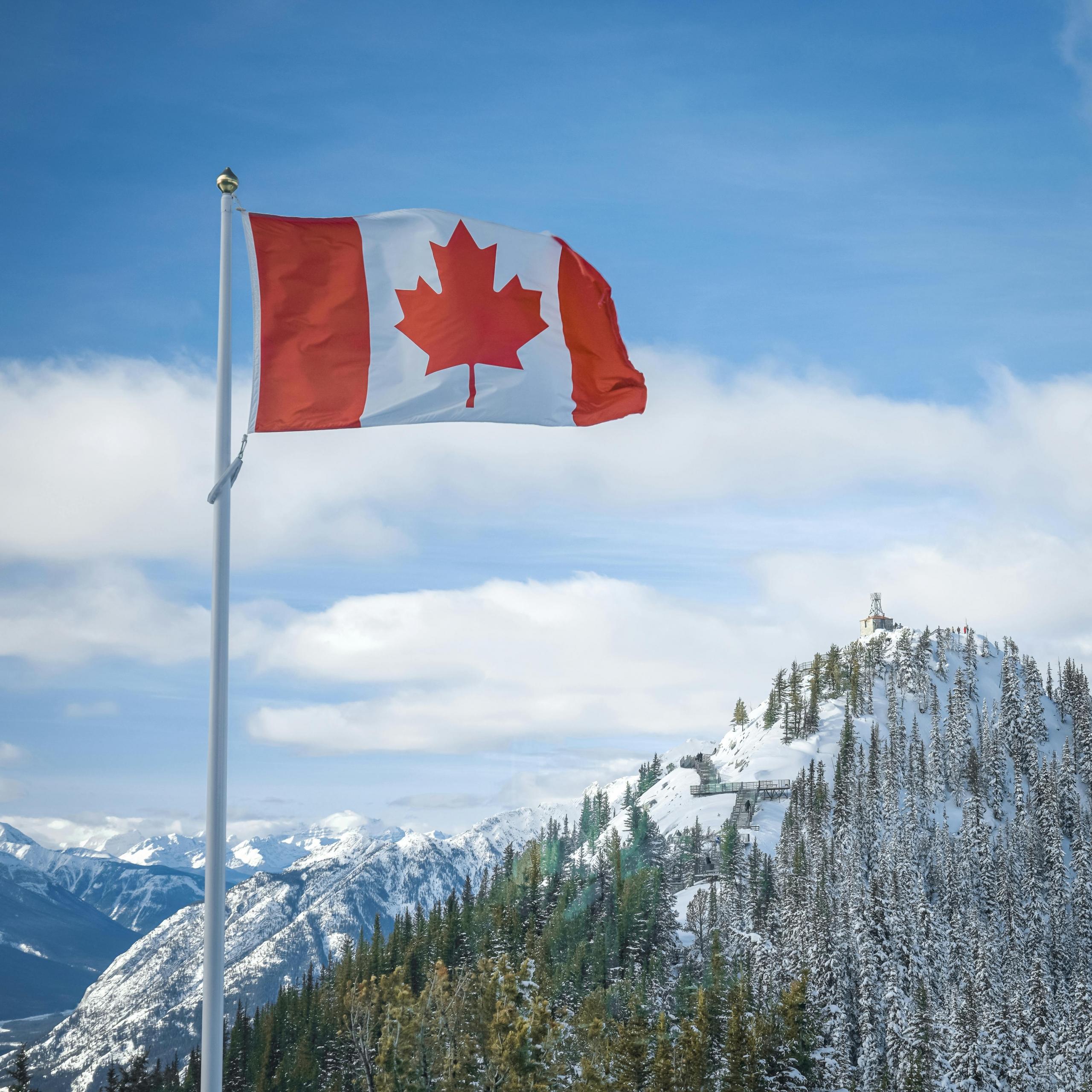 a Canadian flag flies with snowy mountains and blue skies in the background.