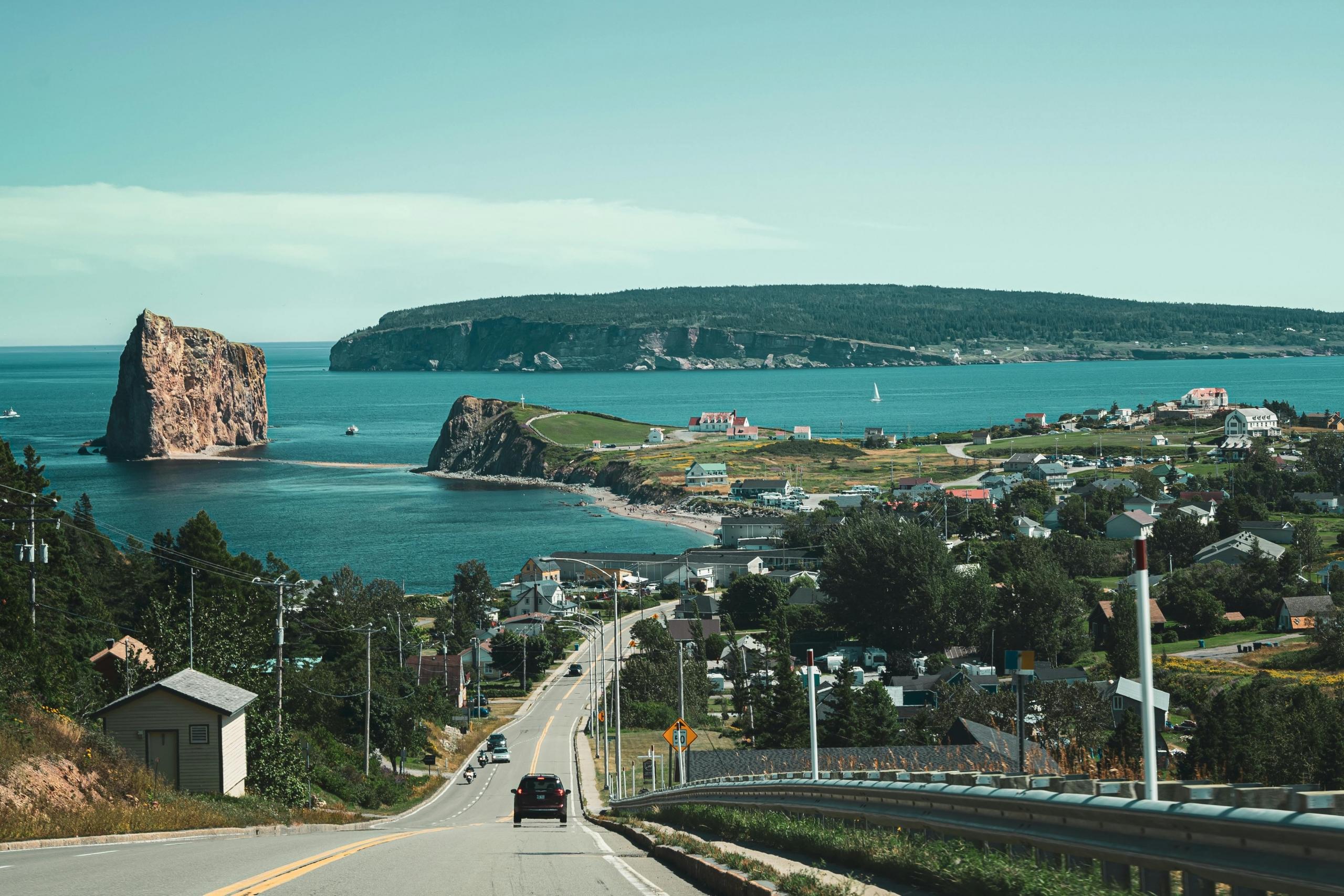 a view of a coastal town from the road. A large rock can be seen jutting in the sea.