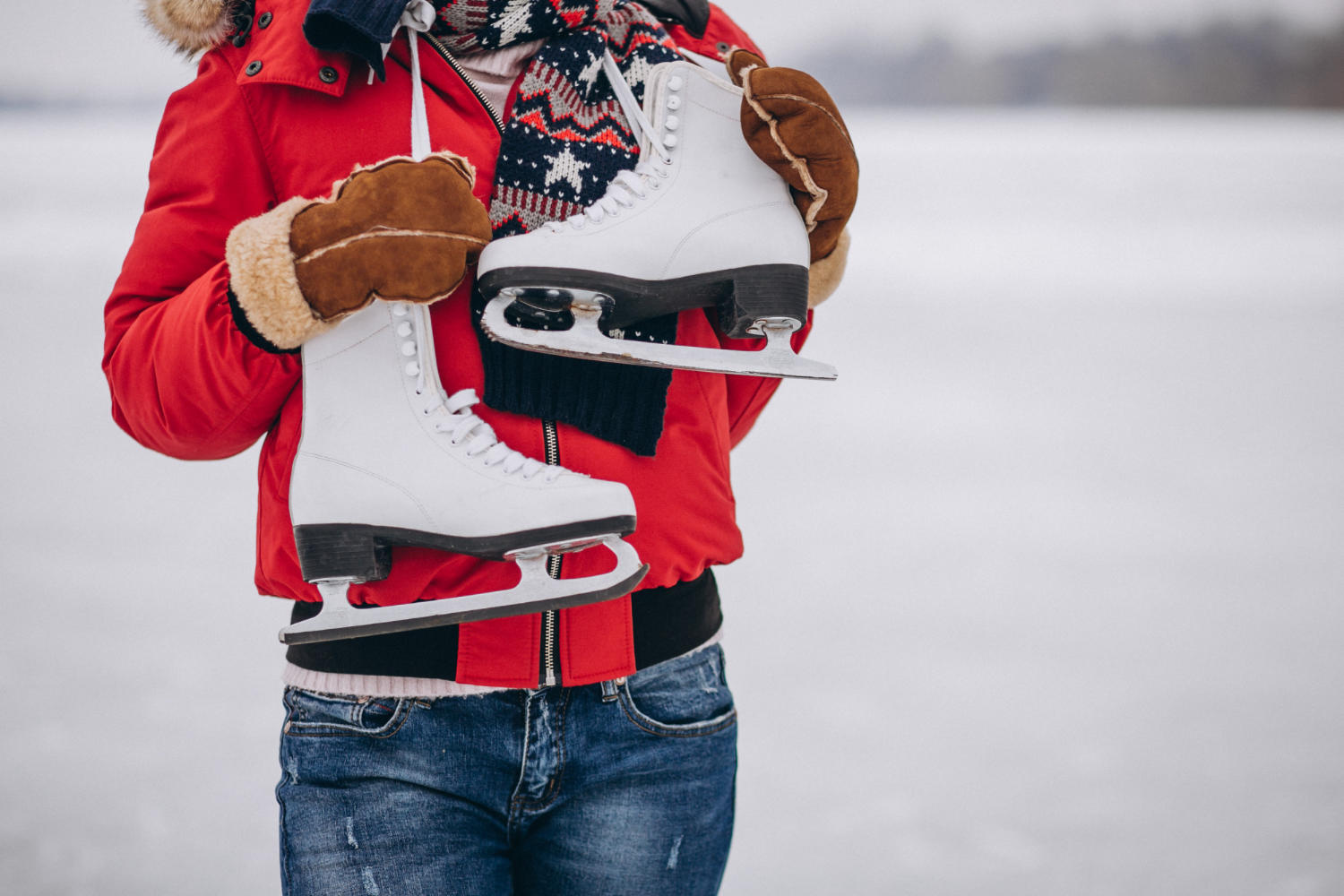 A woman holding a pair of skates with a snowy background.
