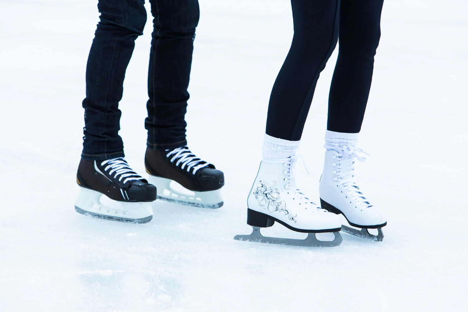 Two people ice skating, one in black skates and one in white skates.