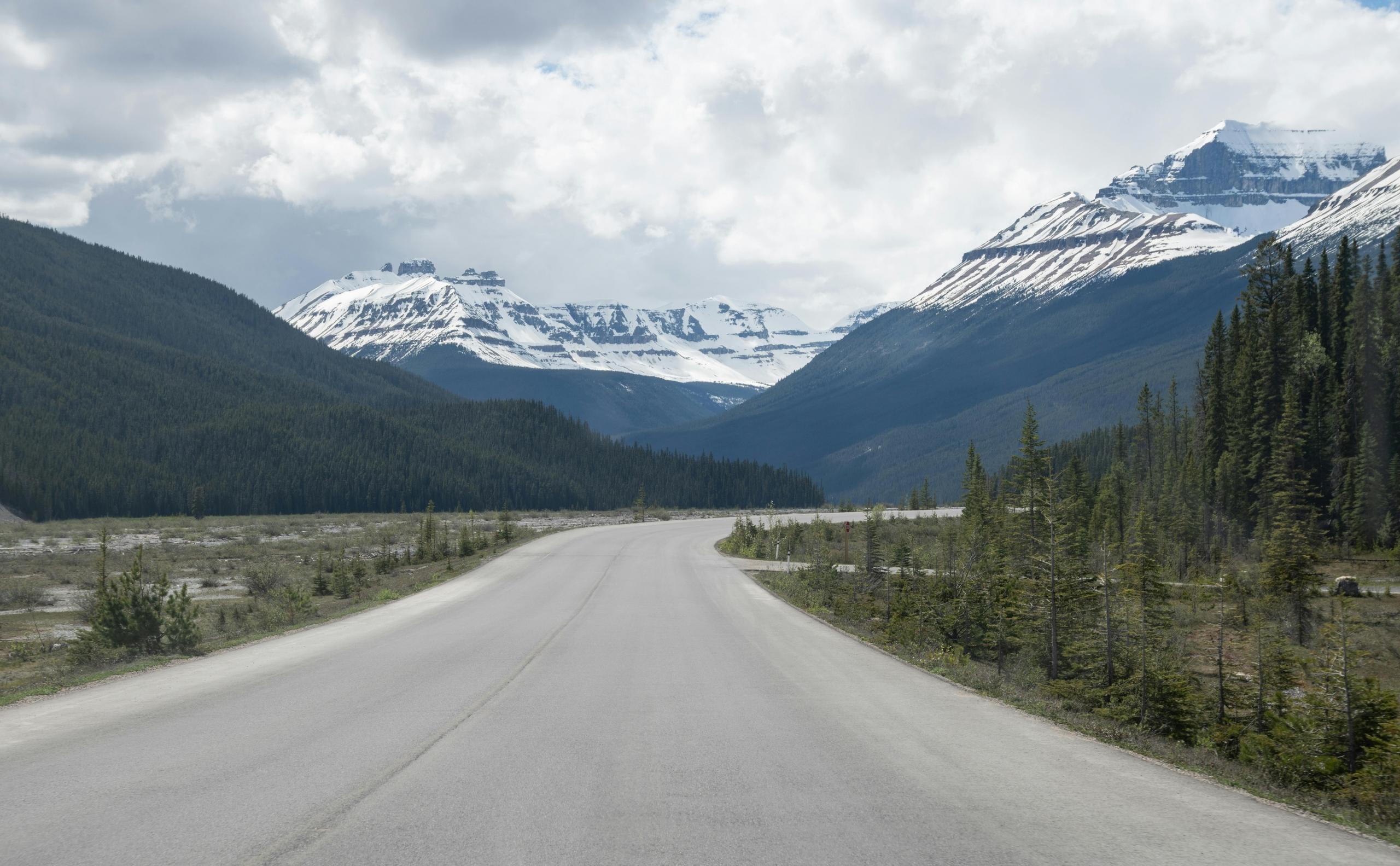 a road leads into snowy mountains. The sky is cloudy.