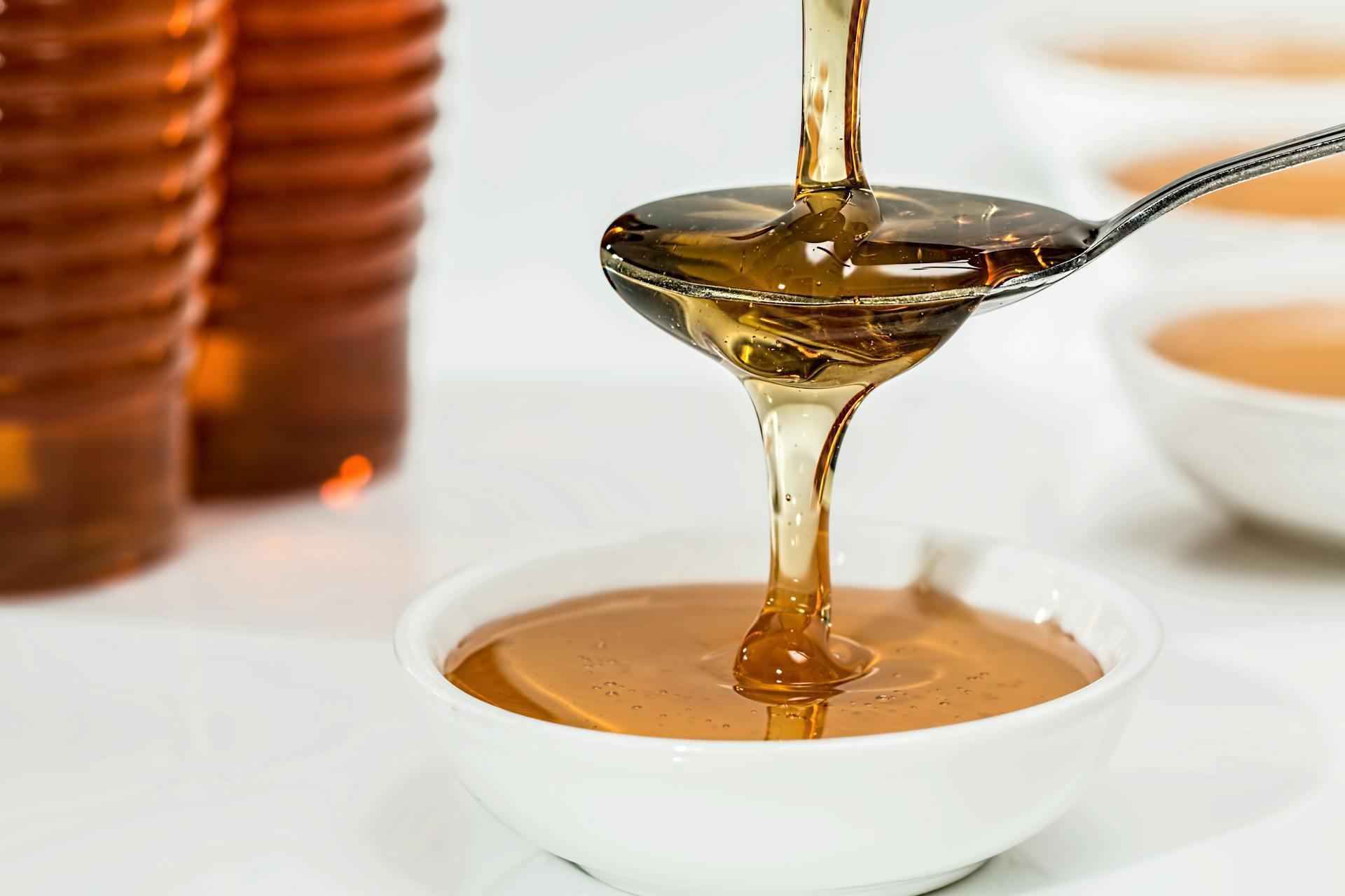 Photograph showing maple syrup being poured over a spoon and draining out of it into a small container.