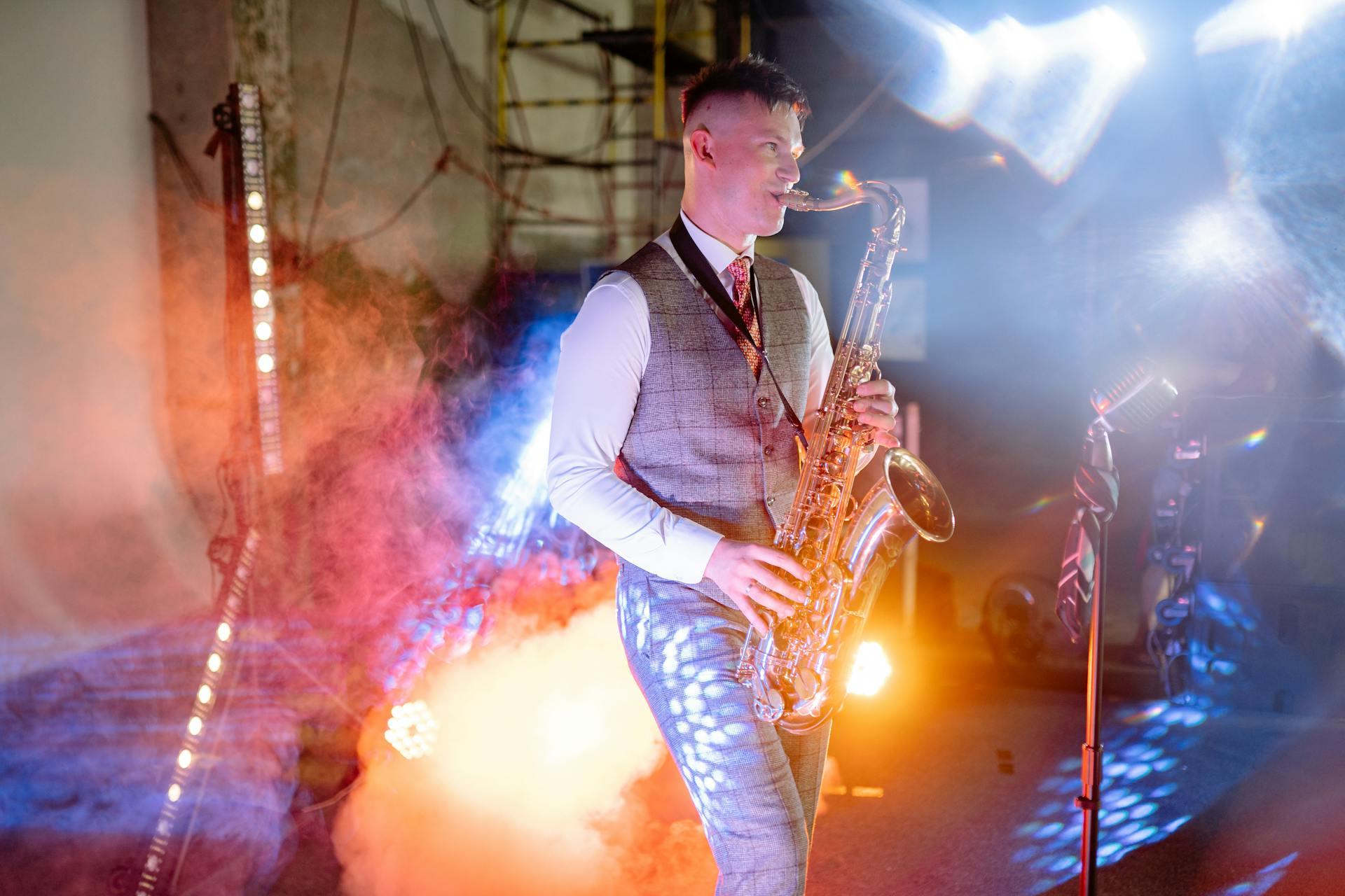The photograph shows a musician, playing the saxophone on a stage with lights in the background. 