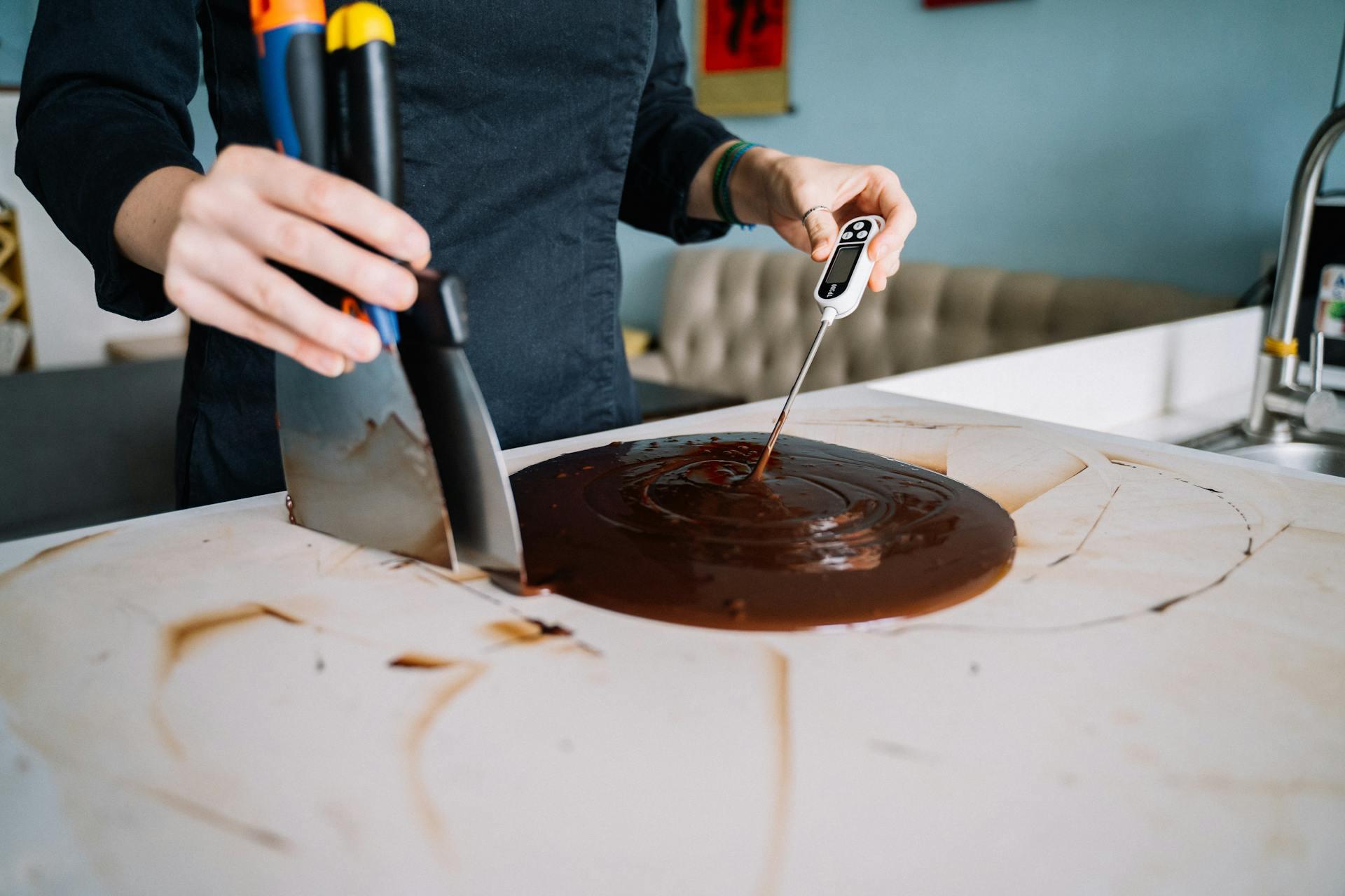 The picture shows a pastry chef taking the temperature of melted chocolate. 