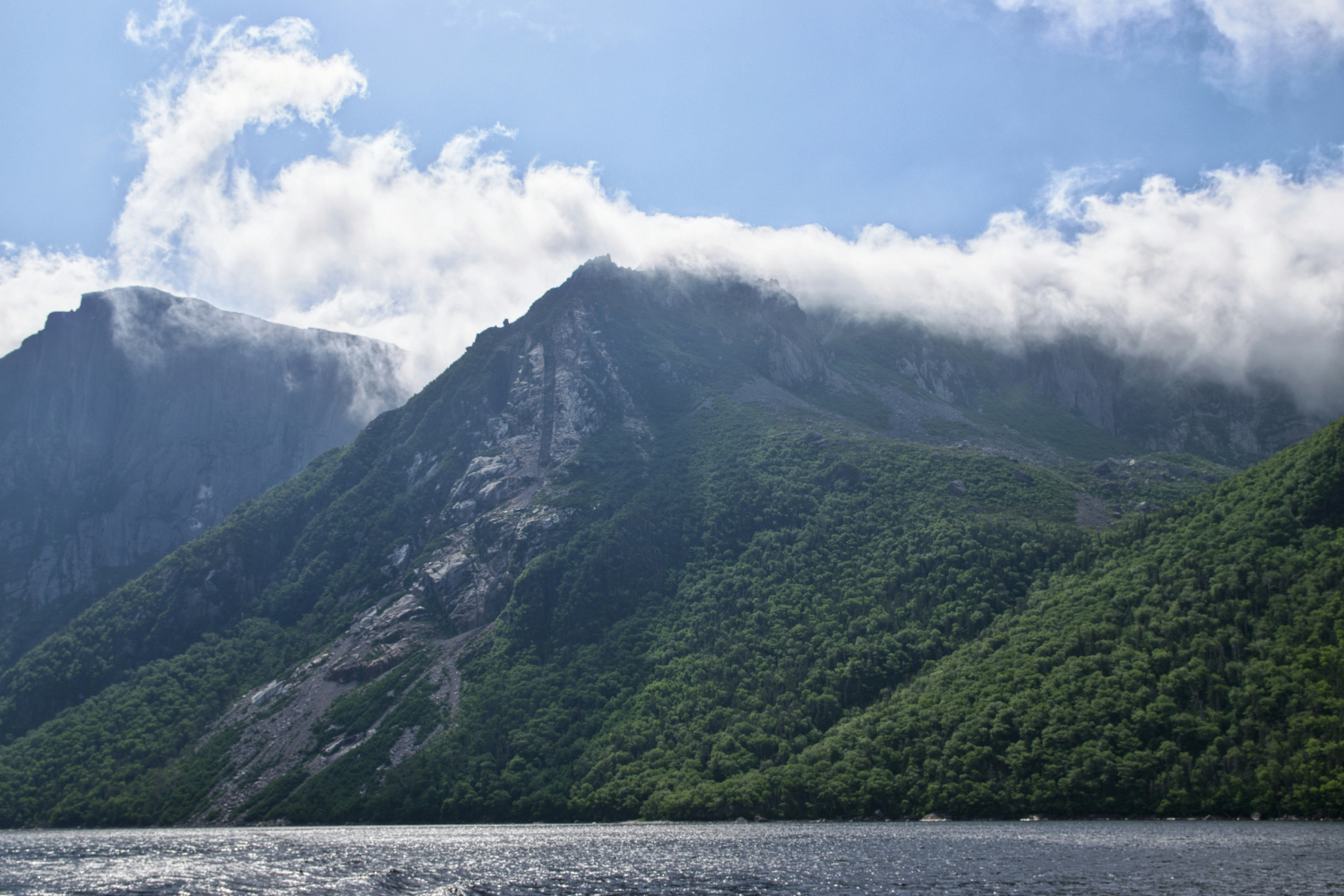 Mountain covered with green forest and low-hanging clouds.
