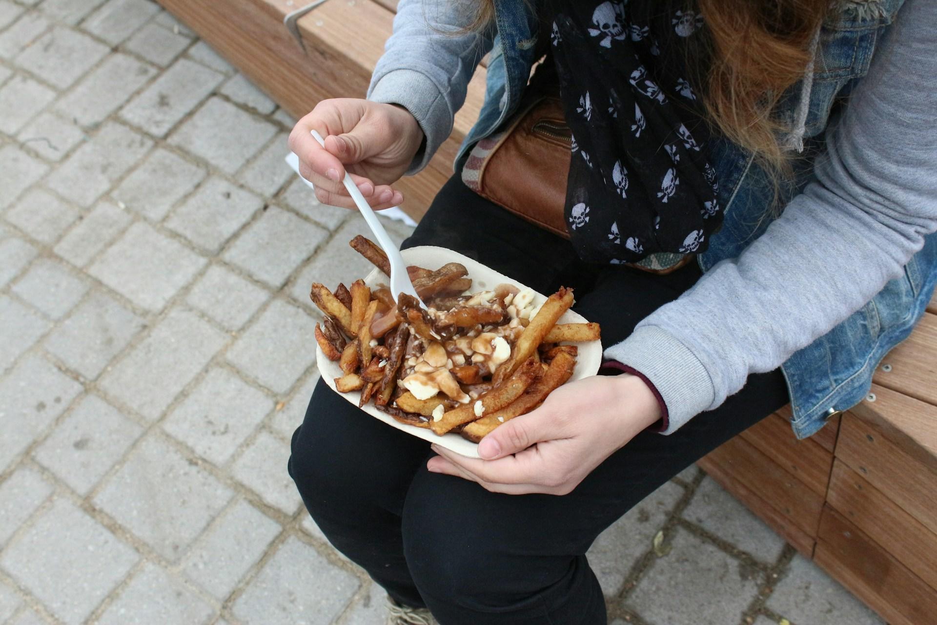 Photo showing a woman enjoying Poutine from a food truck.